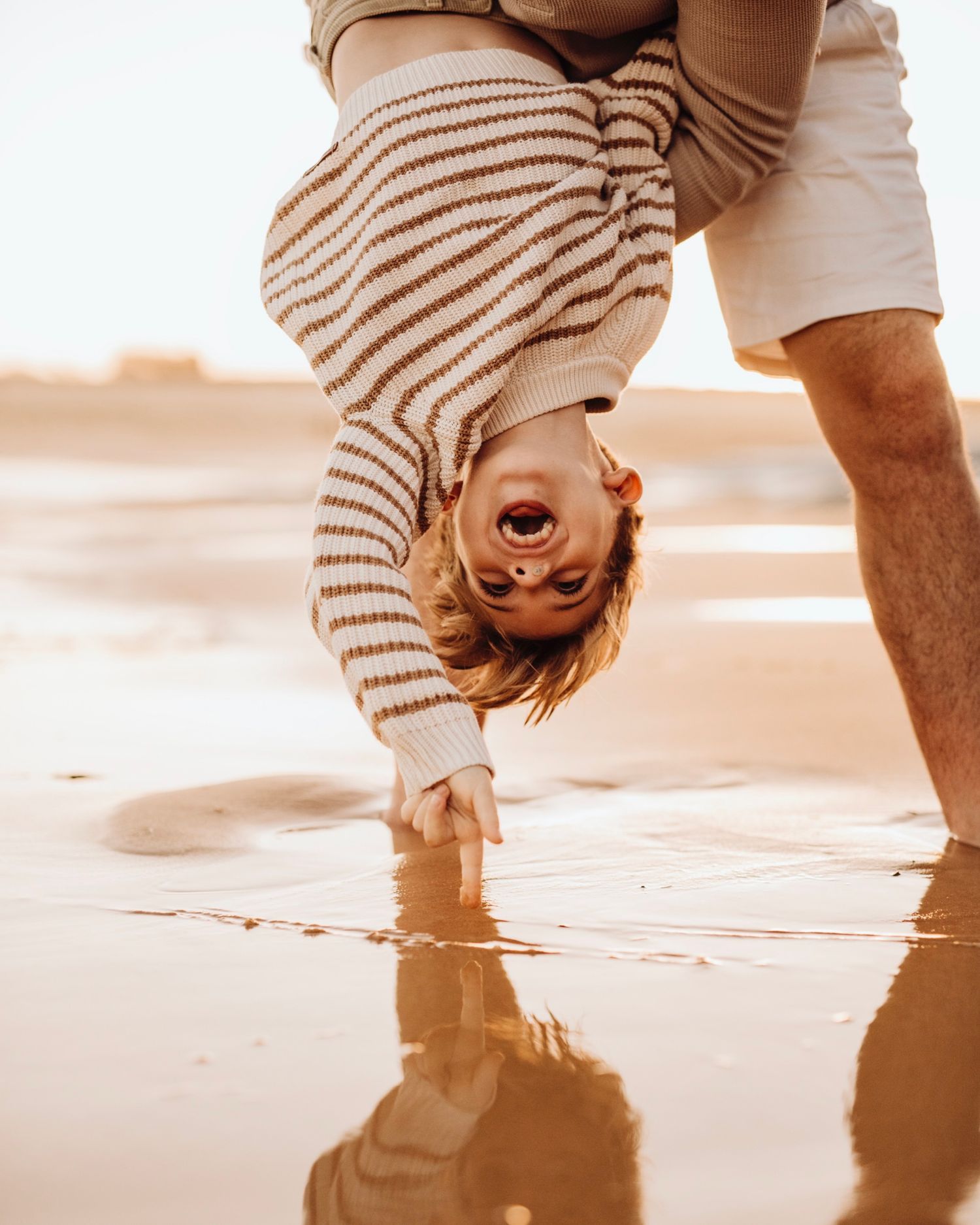 Northern Beaches family photography of mother holding child while father carries another on shoulders by the ocean