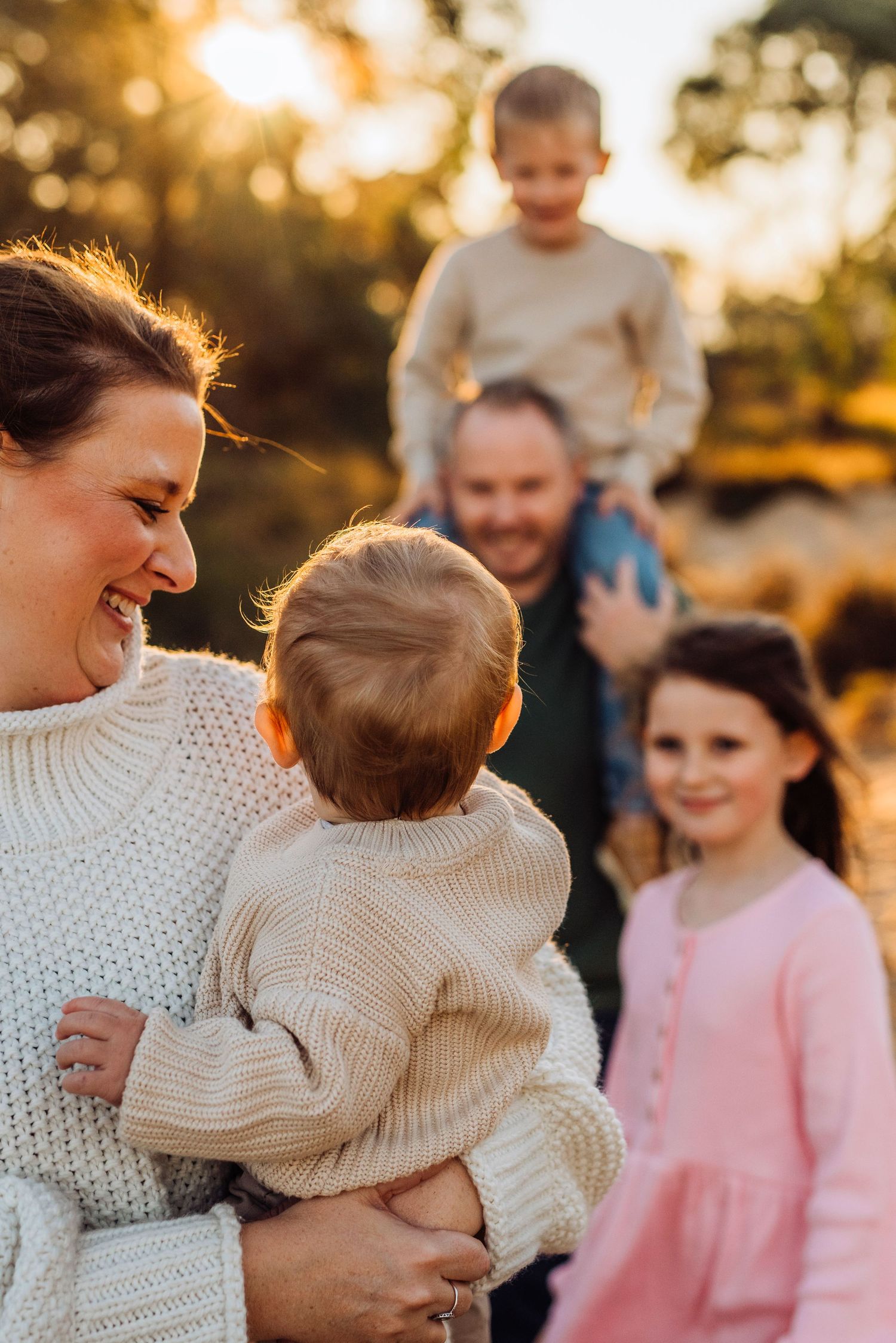 family photography Western Sydney of mother holding baby with family in background, relaxed candid moment outdoors