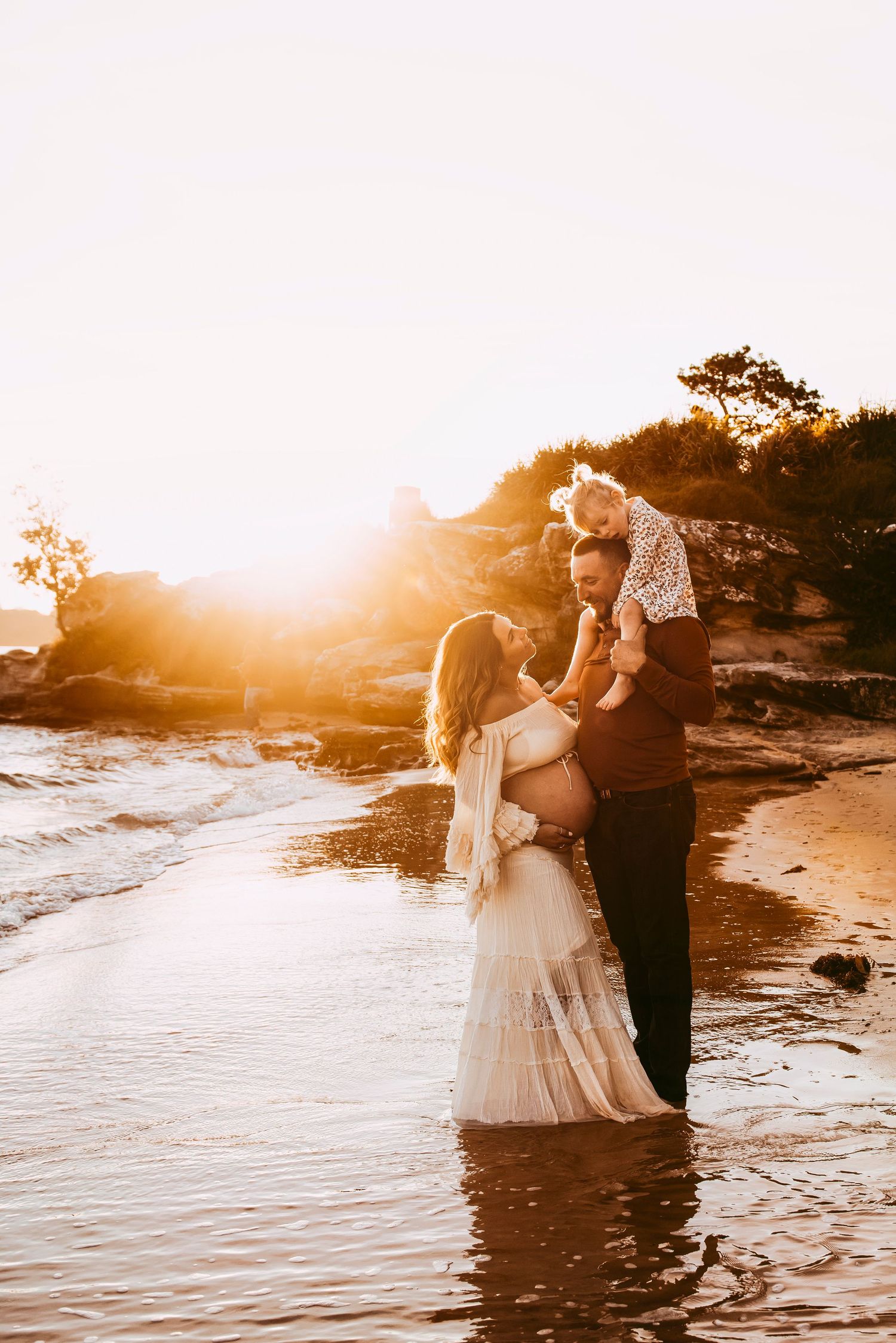 family maternity photography Vaucluse Sydney of parents with toddler and pregnant mother at sunset on Sydney Harbour beach, rainbow baby