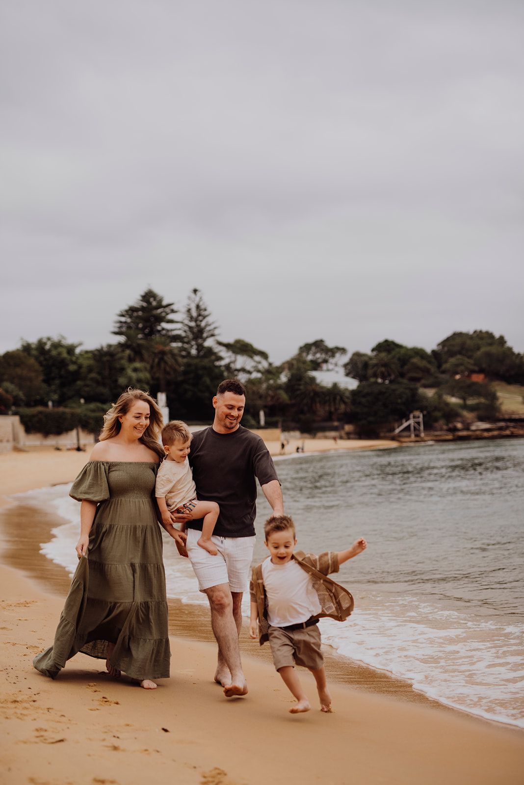 Watsons Bay family photography of parents walking along the beach with two young children at sunset. IVF success