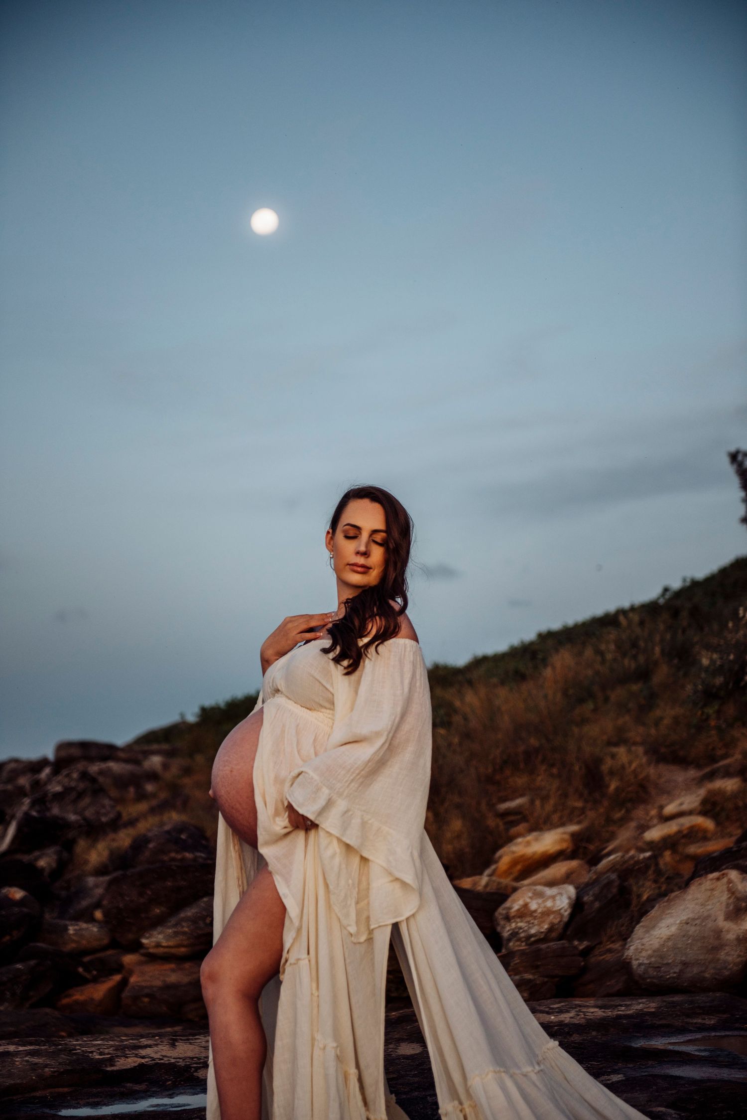 Maternity portrait at dusk in Sydney with mother in flowing gown from Mamarentals under evening sky