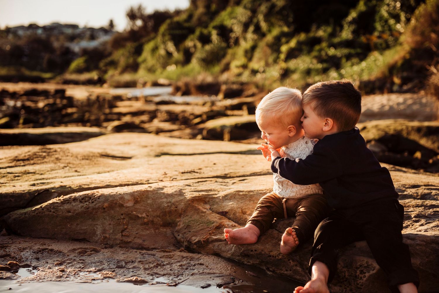 Northern Beaches family photography of siblings toddlers sitting together on rocks by the ocean