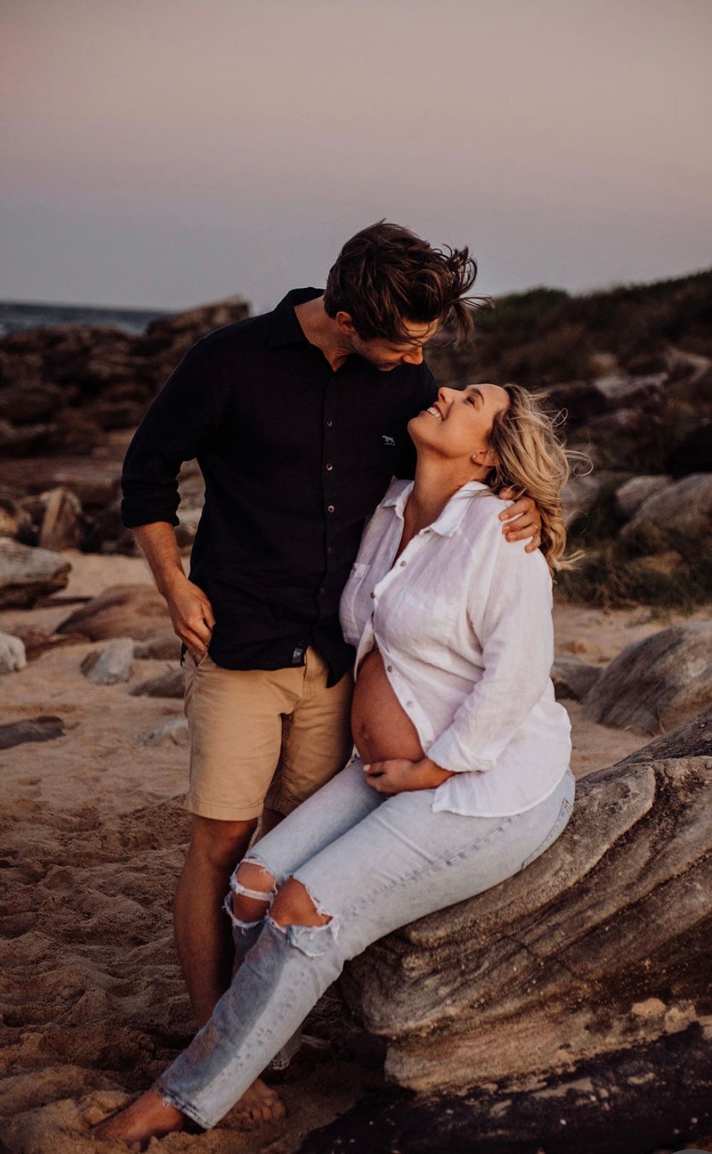 Couple maternity session on rocky Sydney coastline at sunset with natural connection. Awaiting rainbow baby