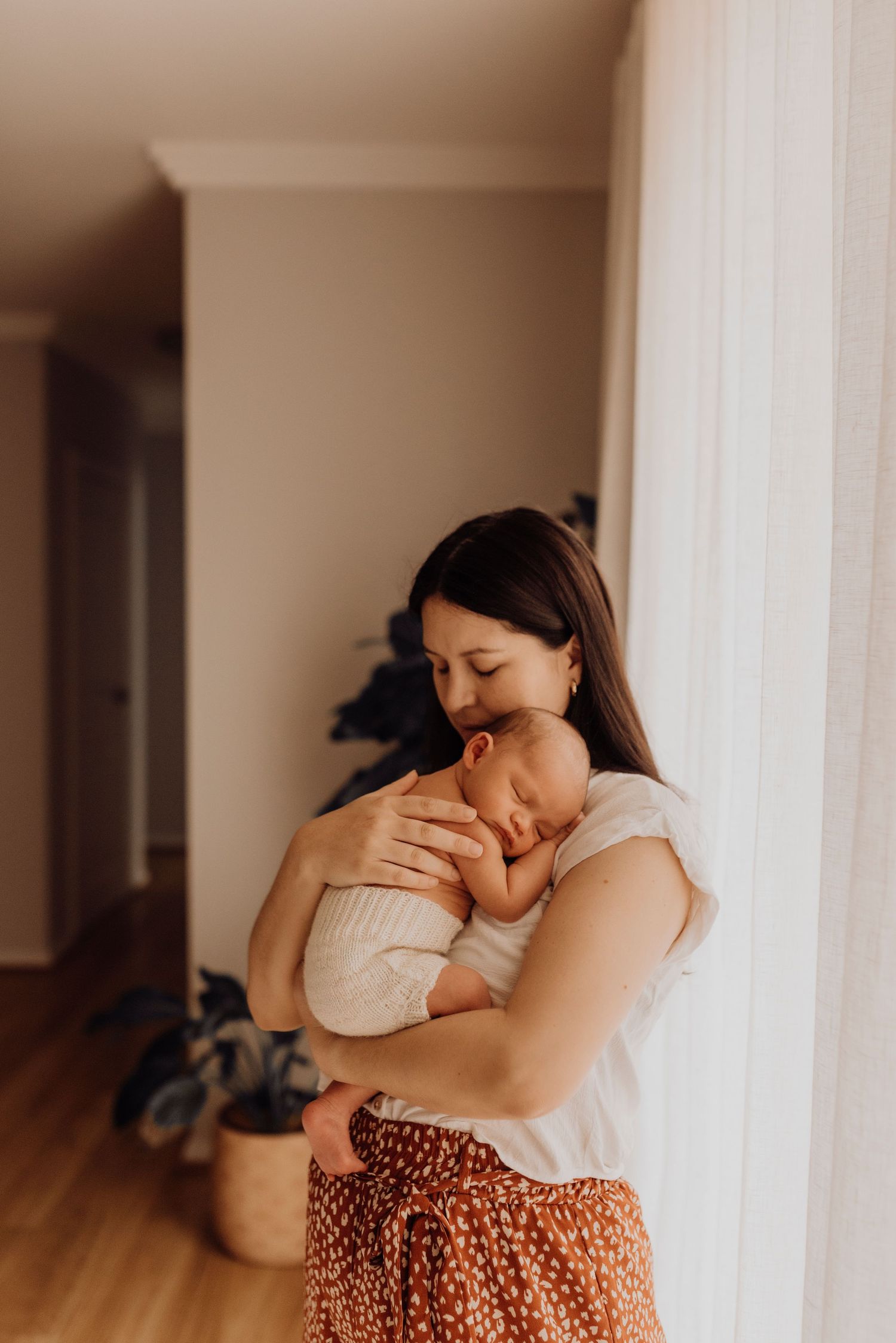 in-home newborn photography Sydney of mother holding newborn baby near doorway in soft light