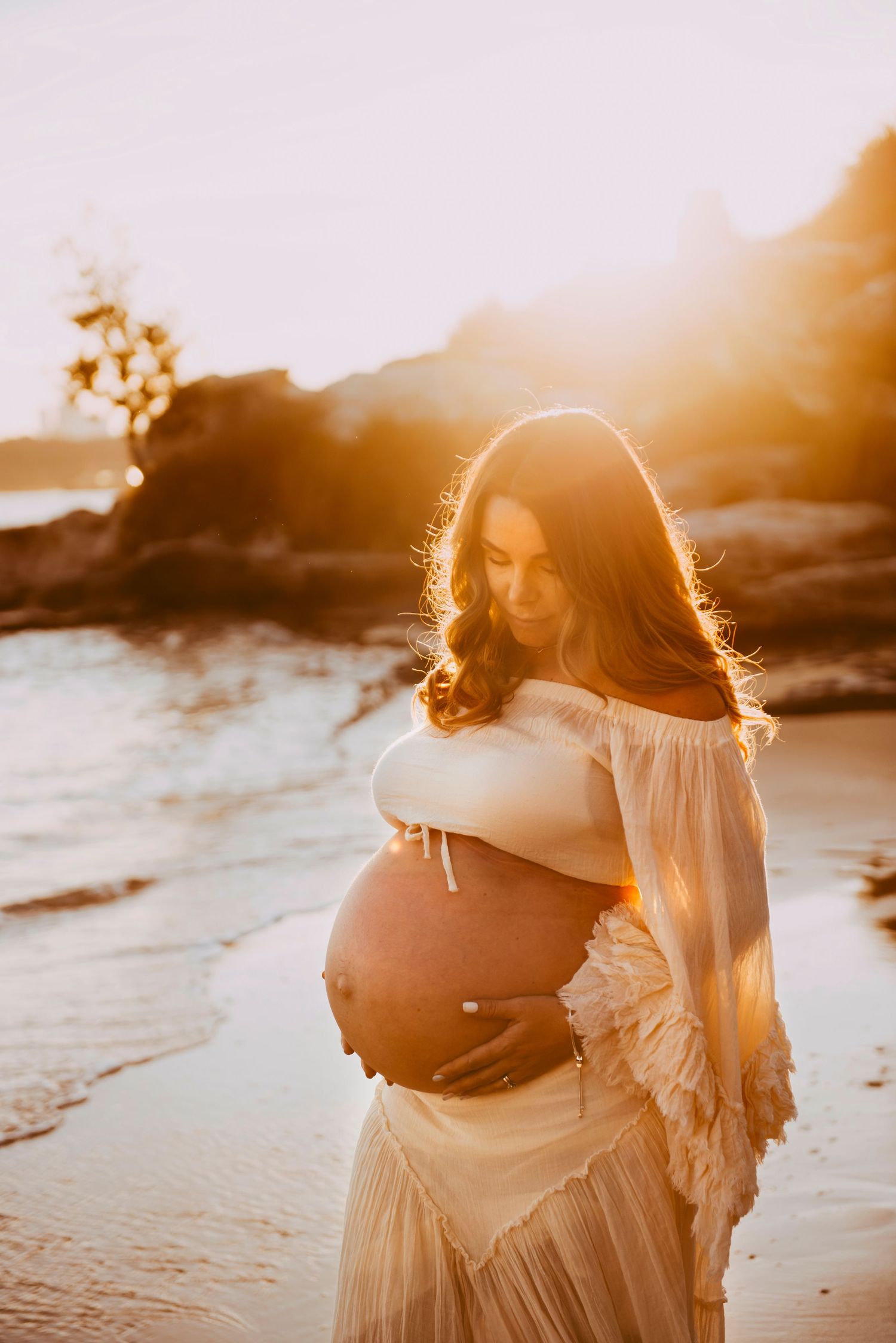 maternity photography Vaucluse Sydney of couple embracing pregnant mother at sunset on Sydney Harbour beach, rainbow baby