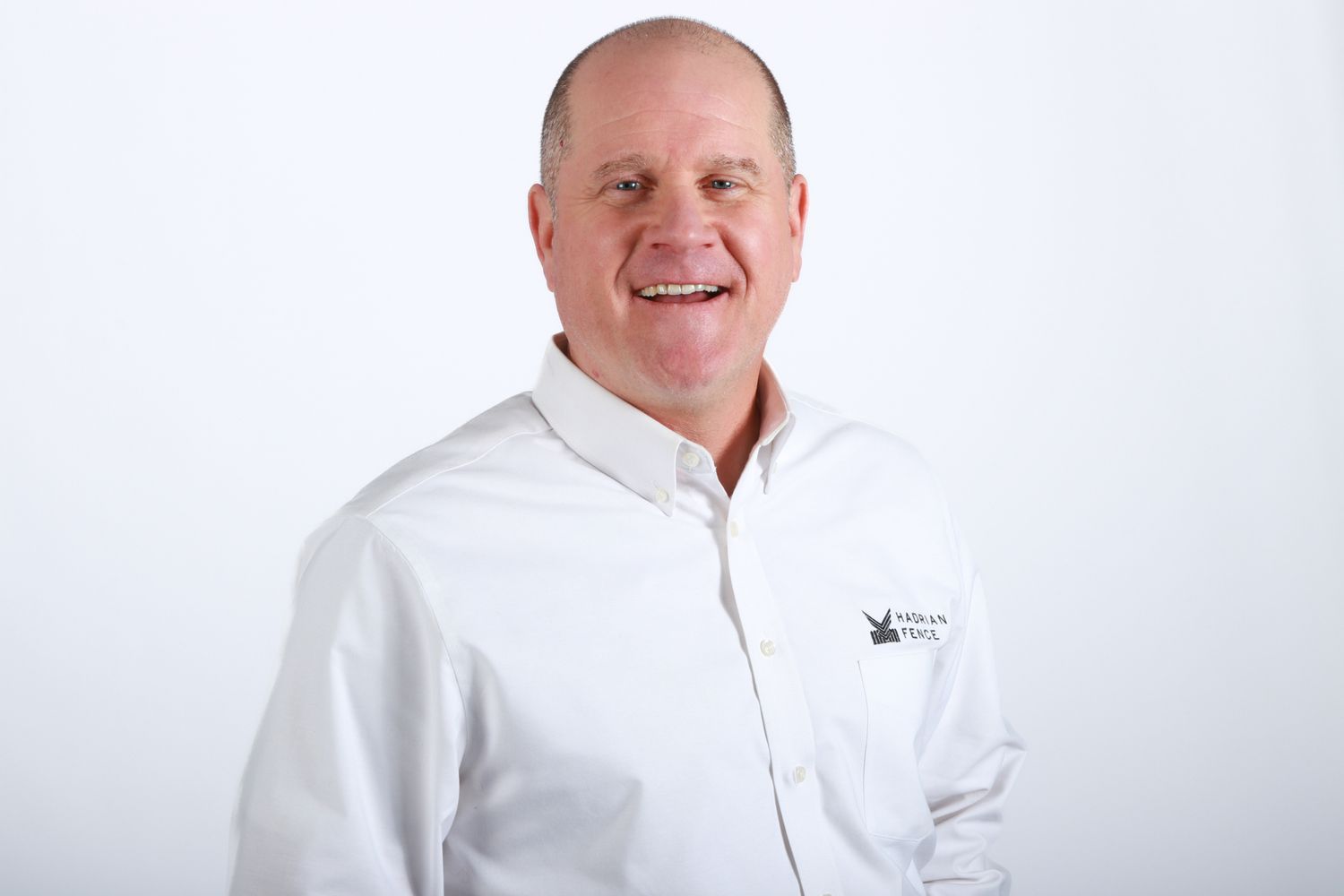 Smiling middle-aged man in white button-down shirt poses for professional corporate headshot portrait.