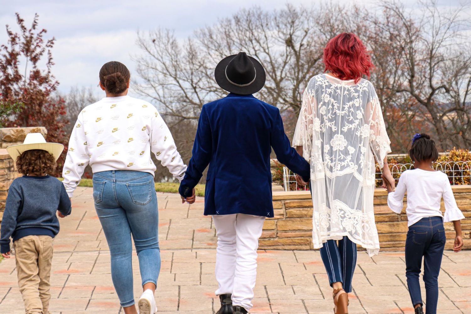 Family of five walking hand in hand away from camera on an outdoor patio.