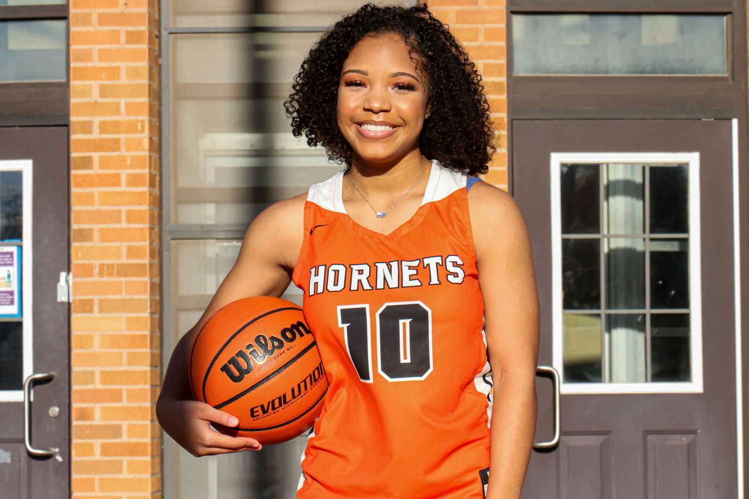 Young female basketball player in orange Hornets jersey number 10 holding a Wilson Evolution ball.