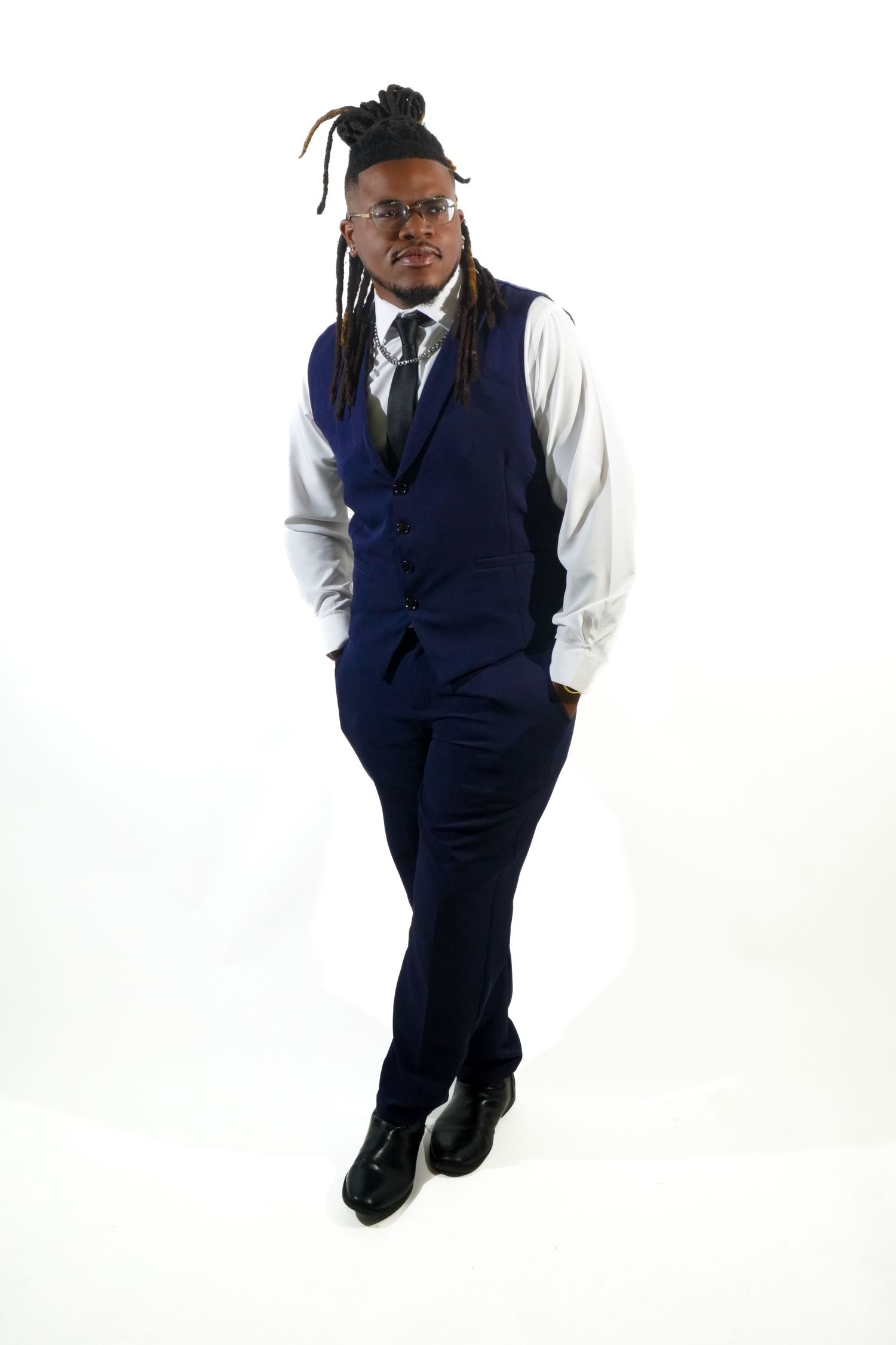 Young man with dreadlocks wearing a navy blue vest suit with white shirt and tie on white background.