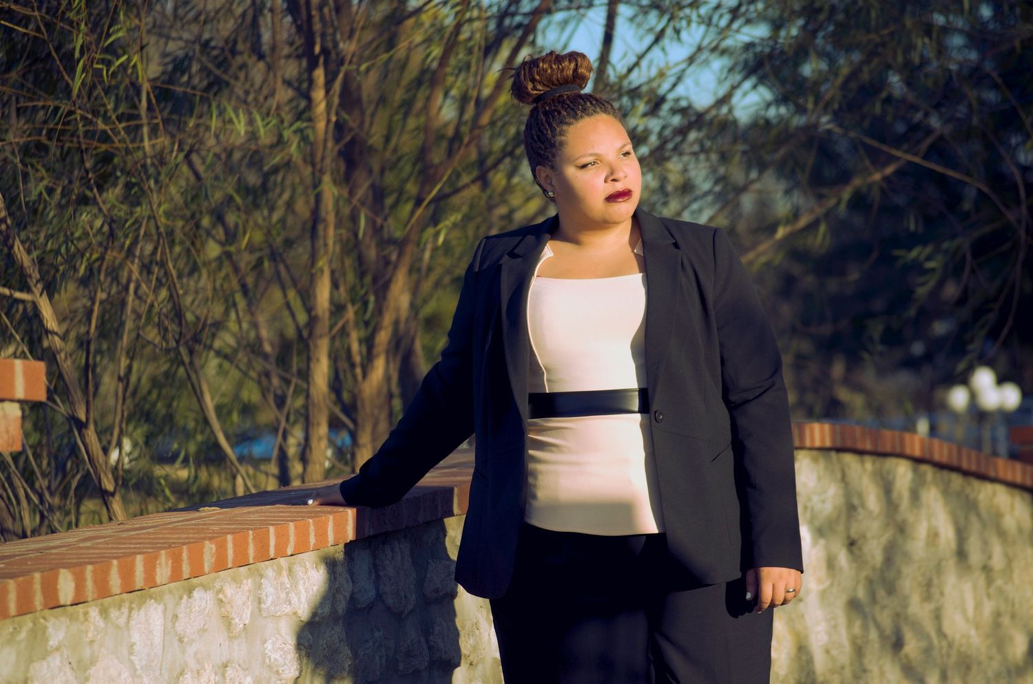 Plus-size woman in black blazer and white top posing outdoors near a brick wall.