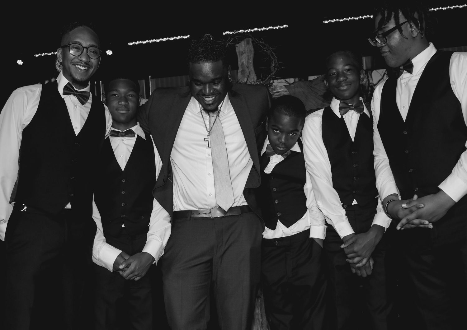 Black and white photo of men and boys in formal vests and bow ties laughing together at a celebration.