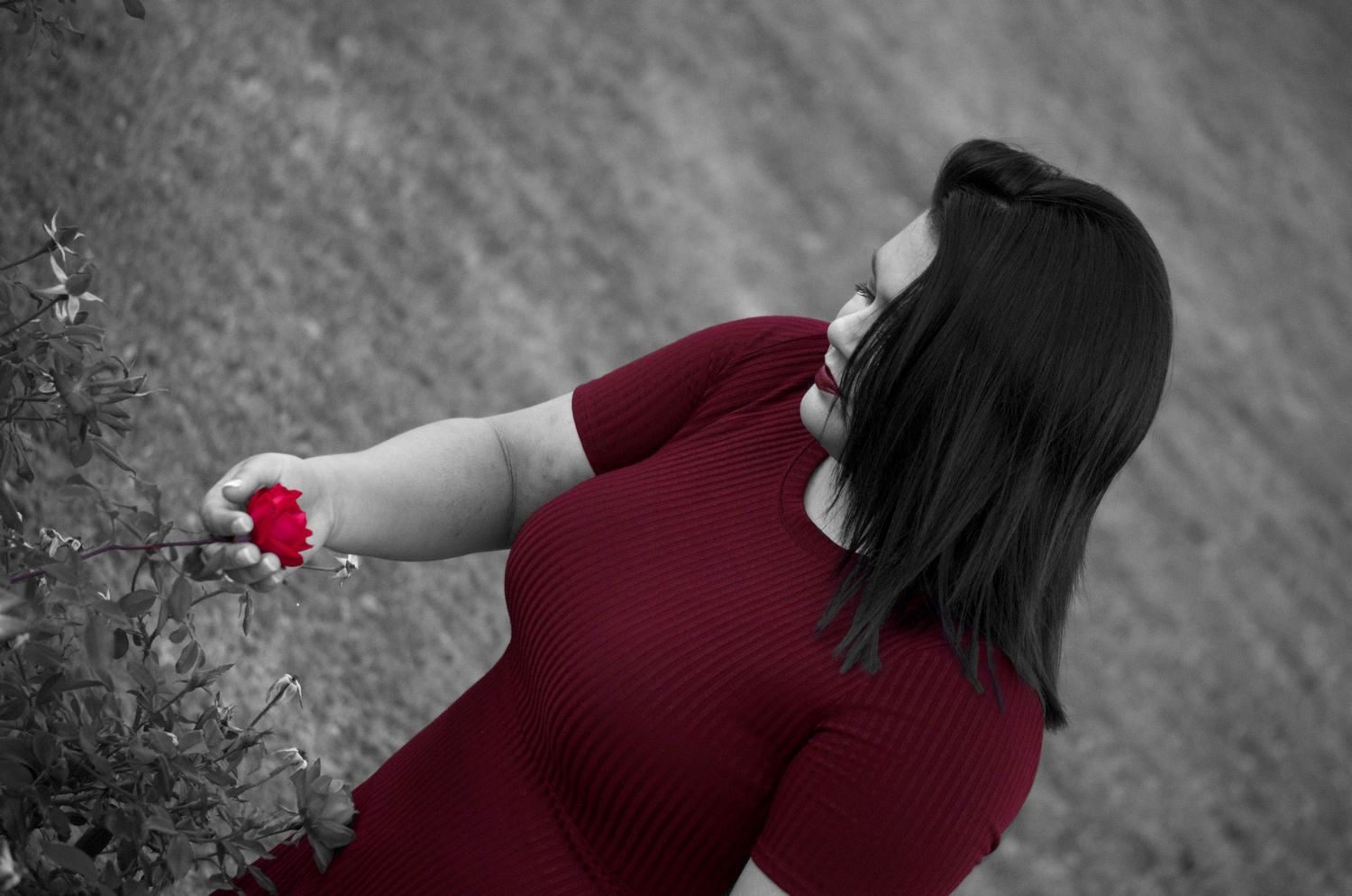 Woman in red dress holding a red rose in a black and white artistic outdoor photo with selective color.