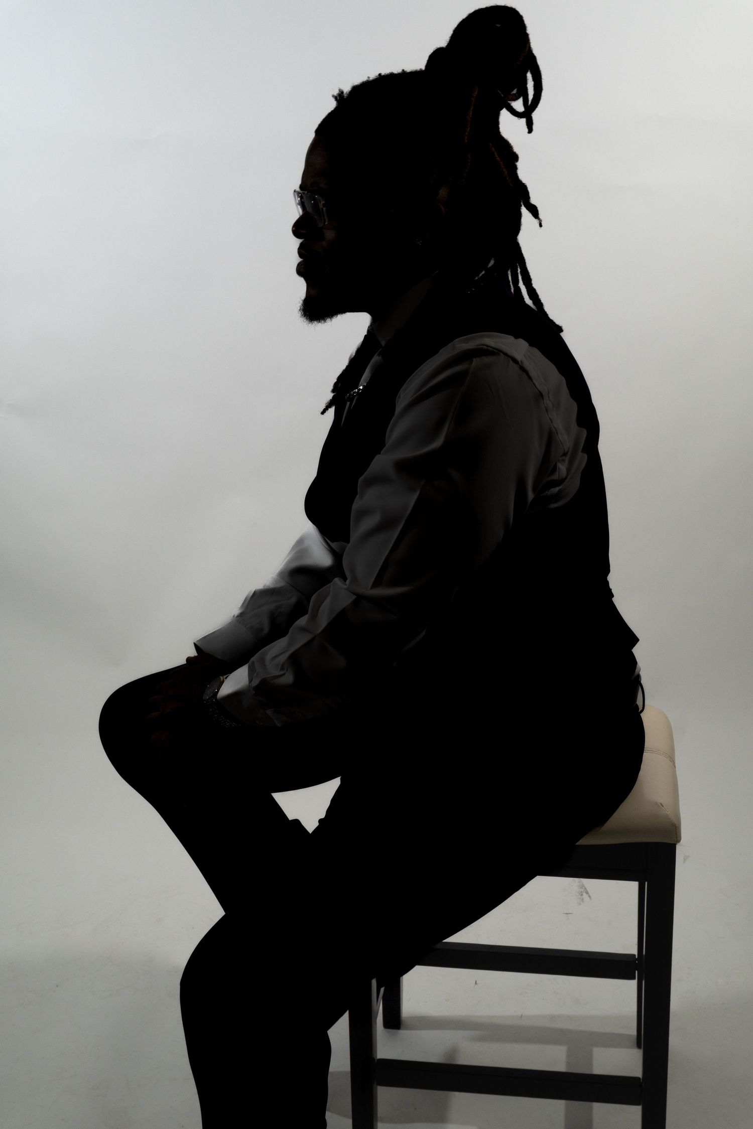 Silhouette of a person with dreadlocks sitting on a stool against a white background.