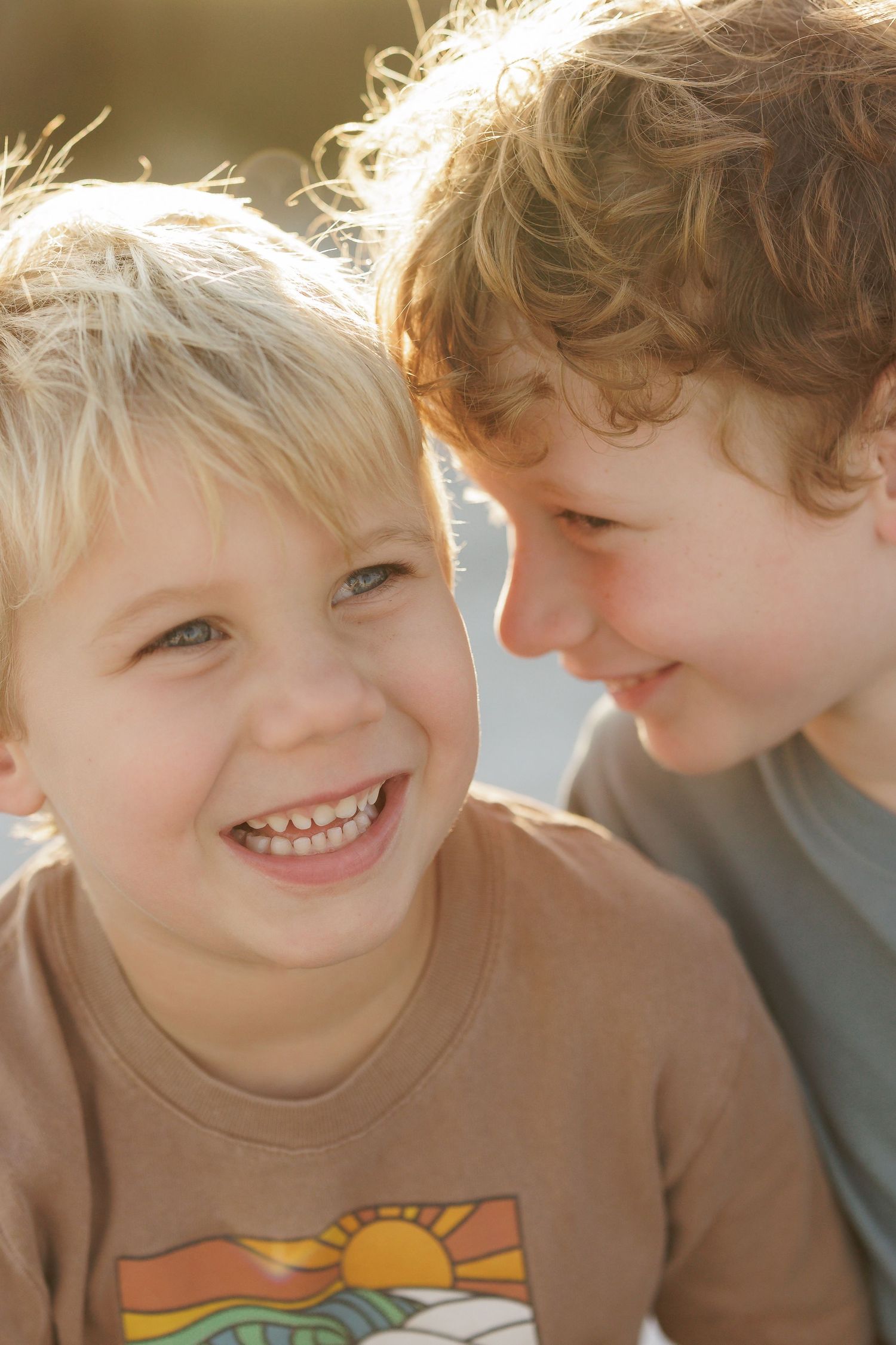 Two children share a joyful moment together with bright smiles in golden sunlight.