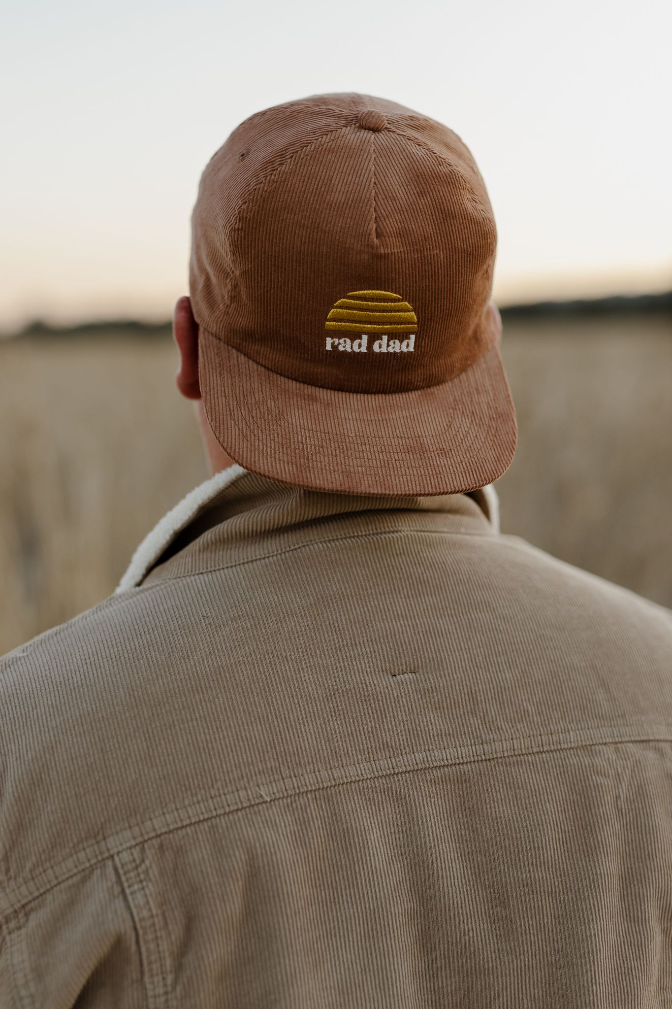 Close-up view of brown corduroy cap with 'rad dad' logo worn backwards.