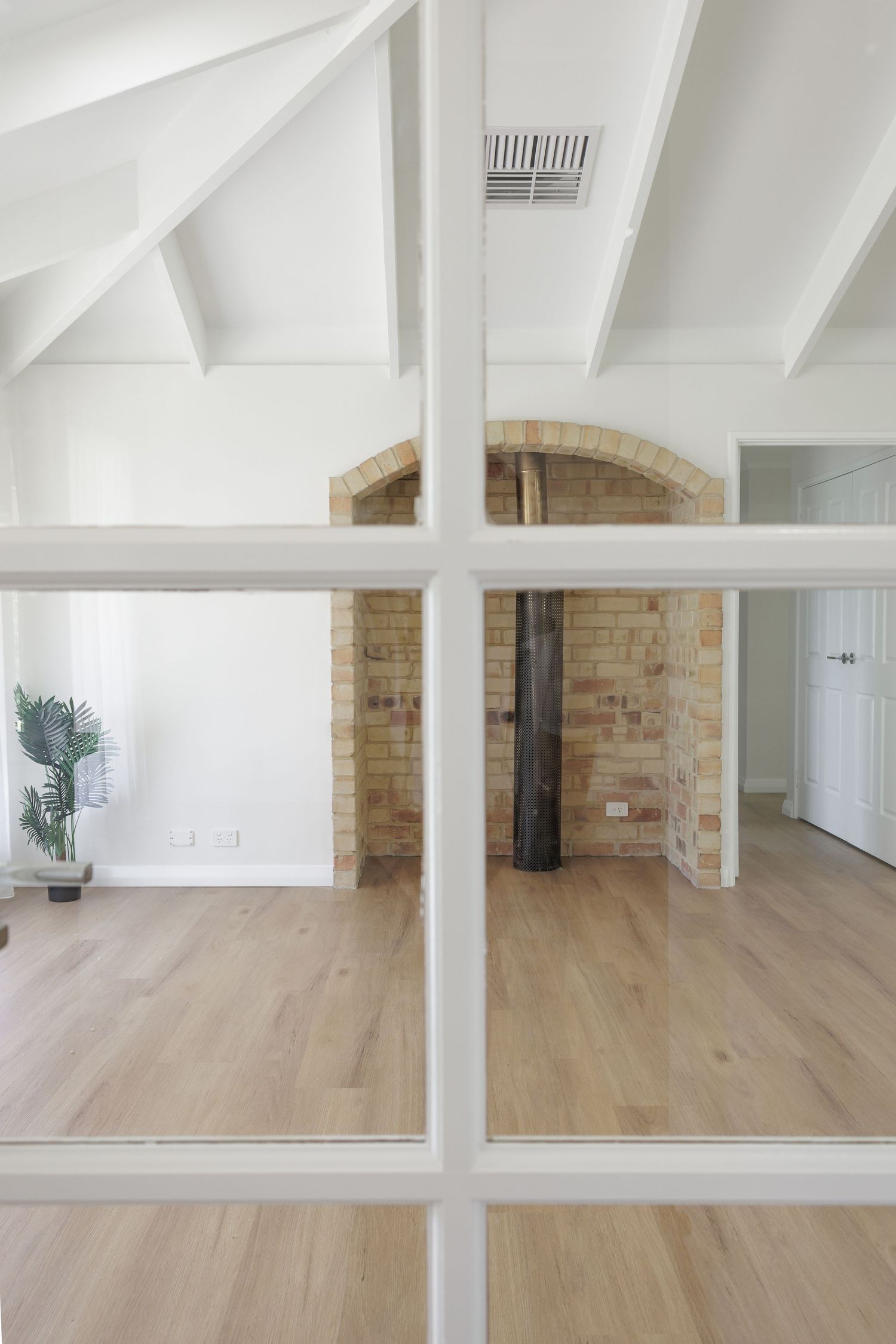 Modern interior space with light hardwood floors, exposed brick walls, and white beamed ceilings.