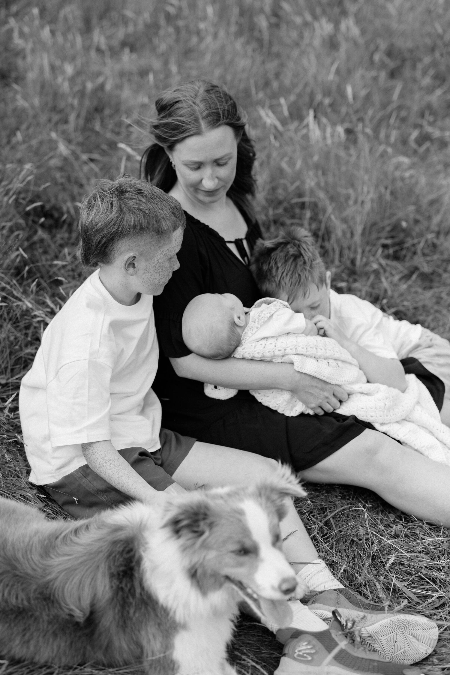 Family relaxing outdoors with their dog in black and white photograph.