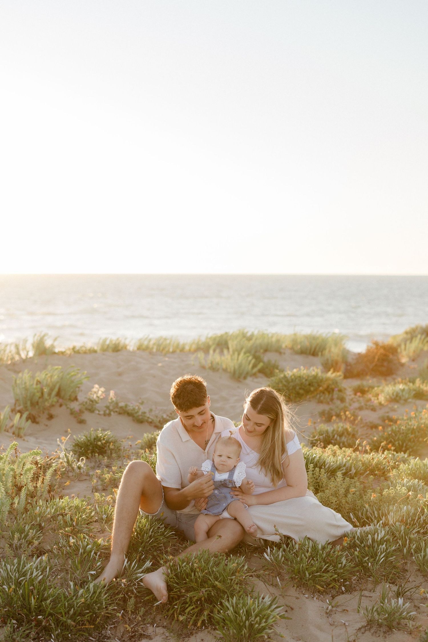 Family enjoying a tender moment together on grassy dunes at sunset.