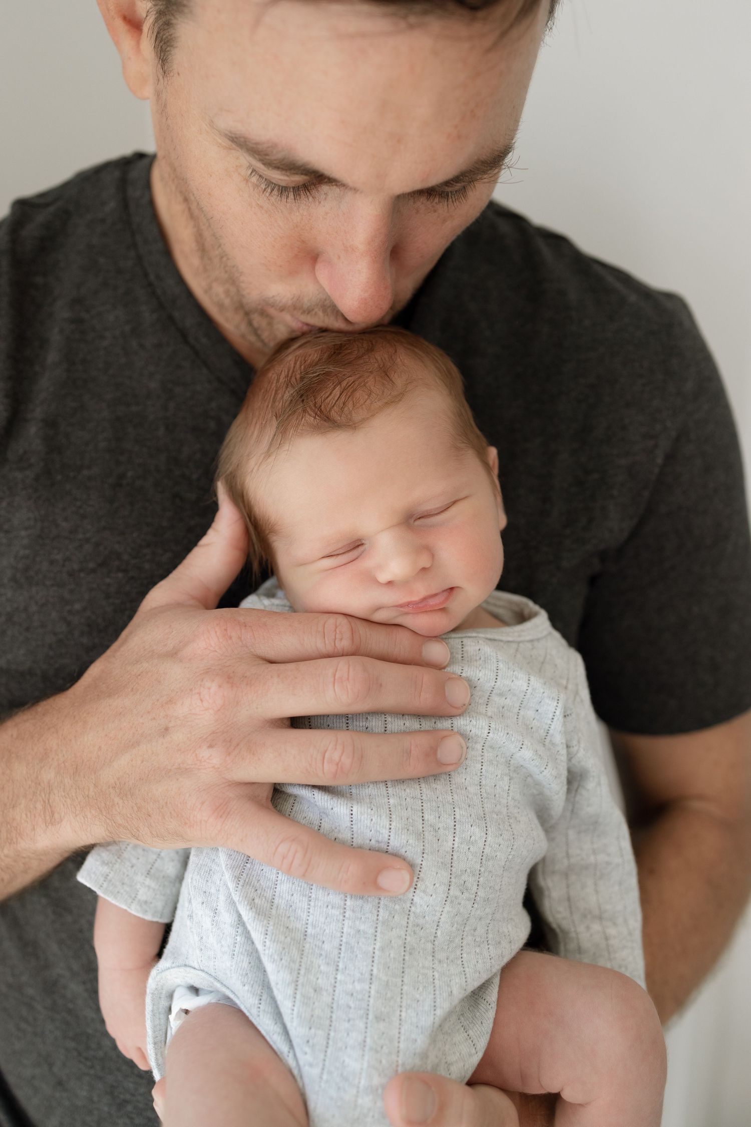 Gentle moment between adult in gray shirt holding sleeping infant in light clothing.