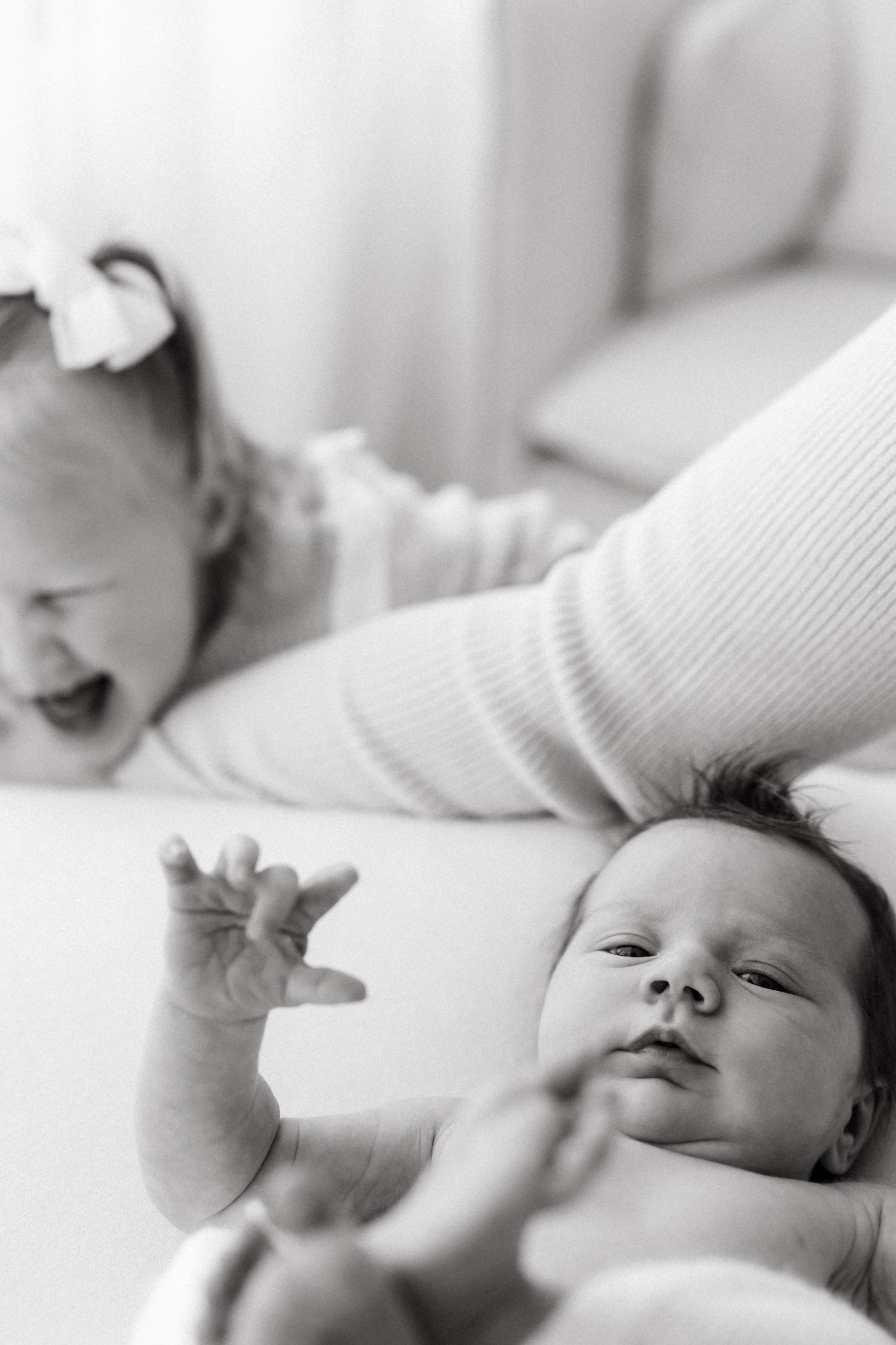 Two babies in white clothing interacting on light colored surface.