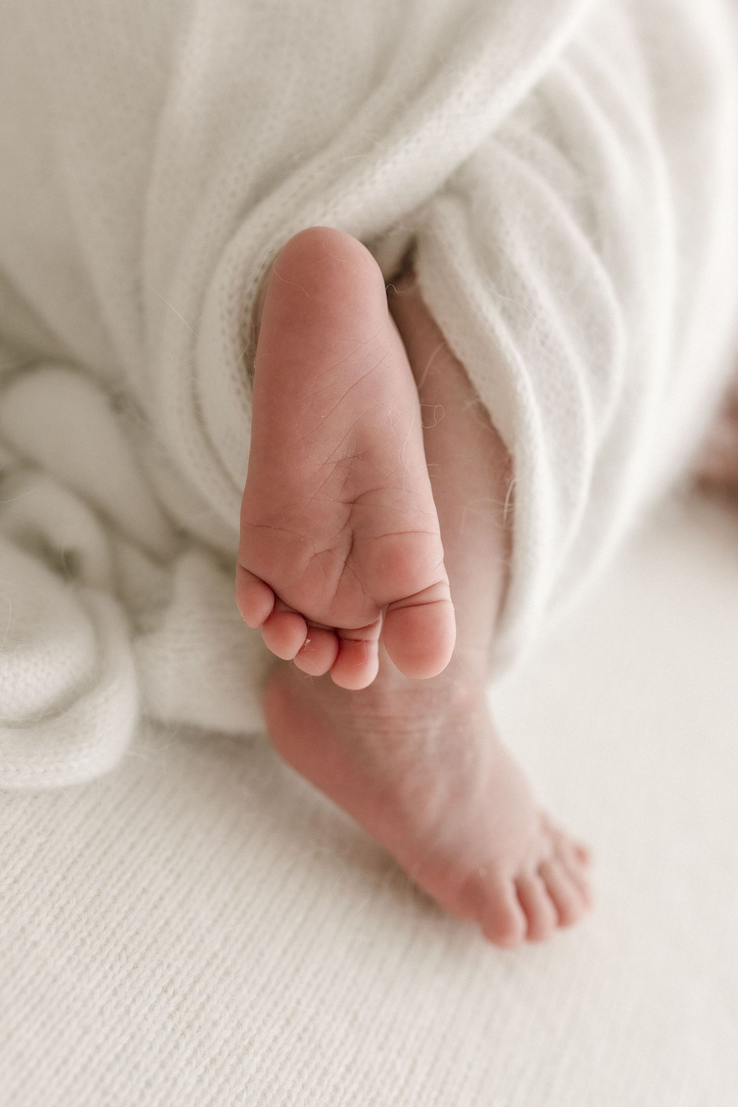 Close-up of baby's foot peeking out from white blanket.