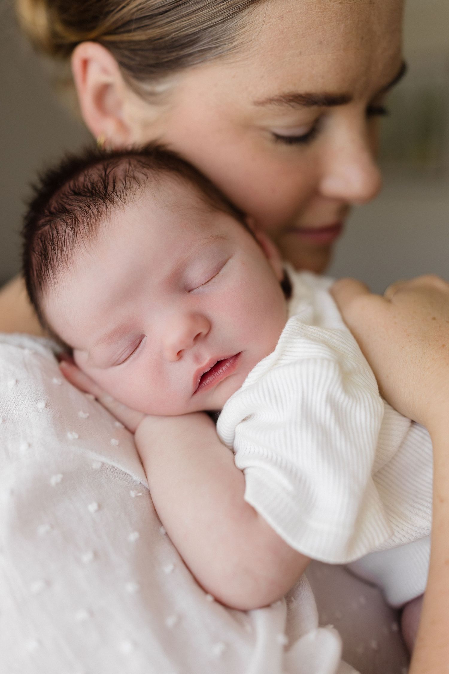 Close-up shots of tender moments with sleeping newborn in white clothing.