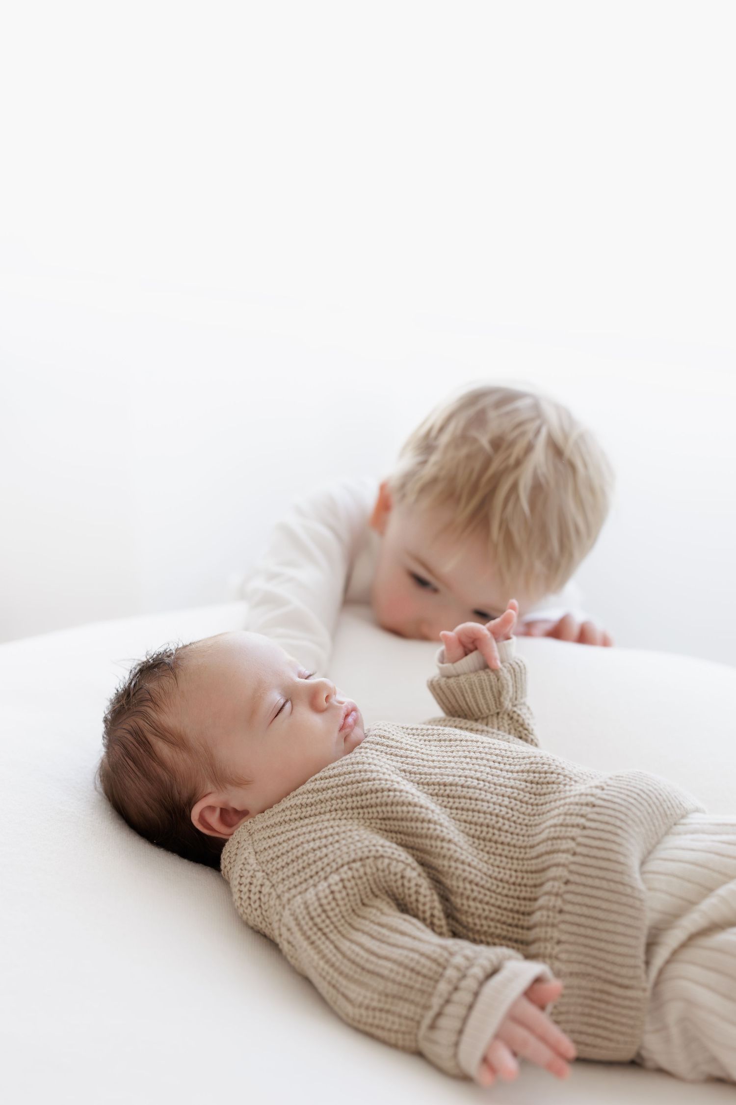 Two children in neutral colored clothing on white background.