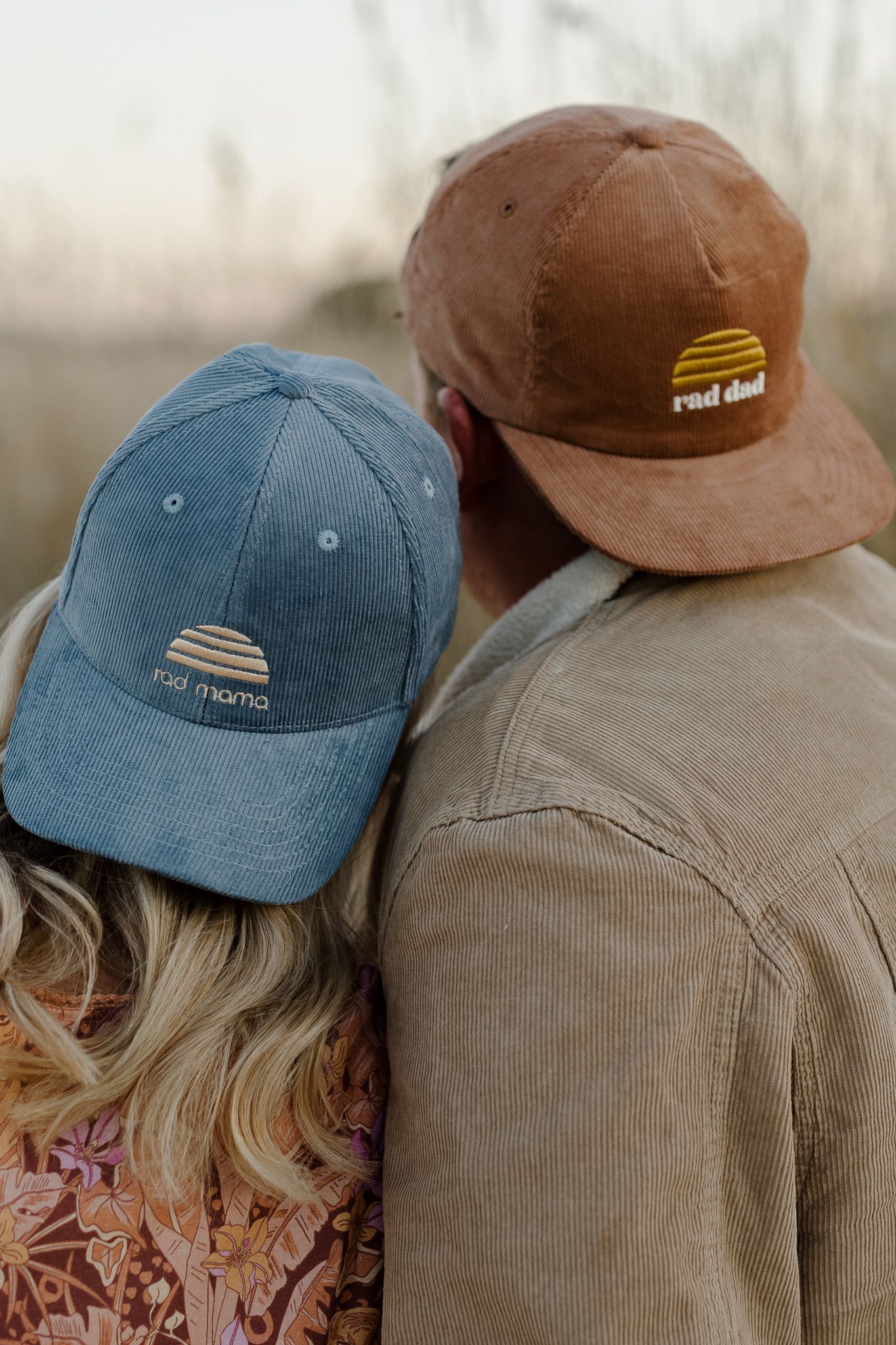 Two corduroy baseball caps, one blue and one brown, shown in close-up detail outdoors.