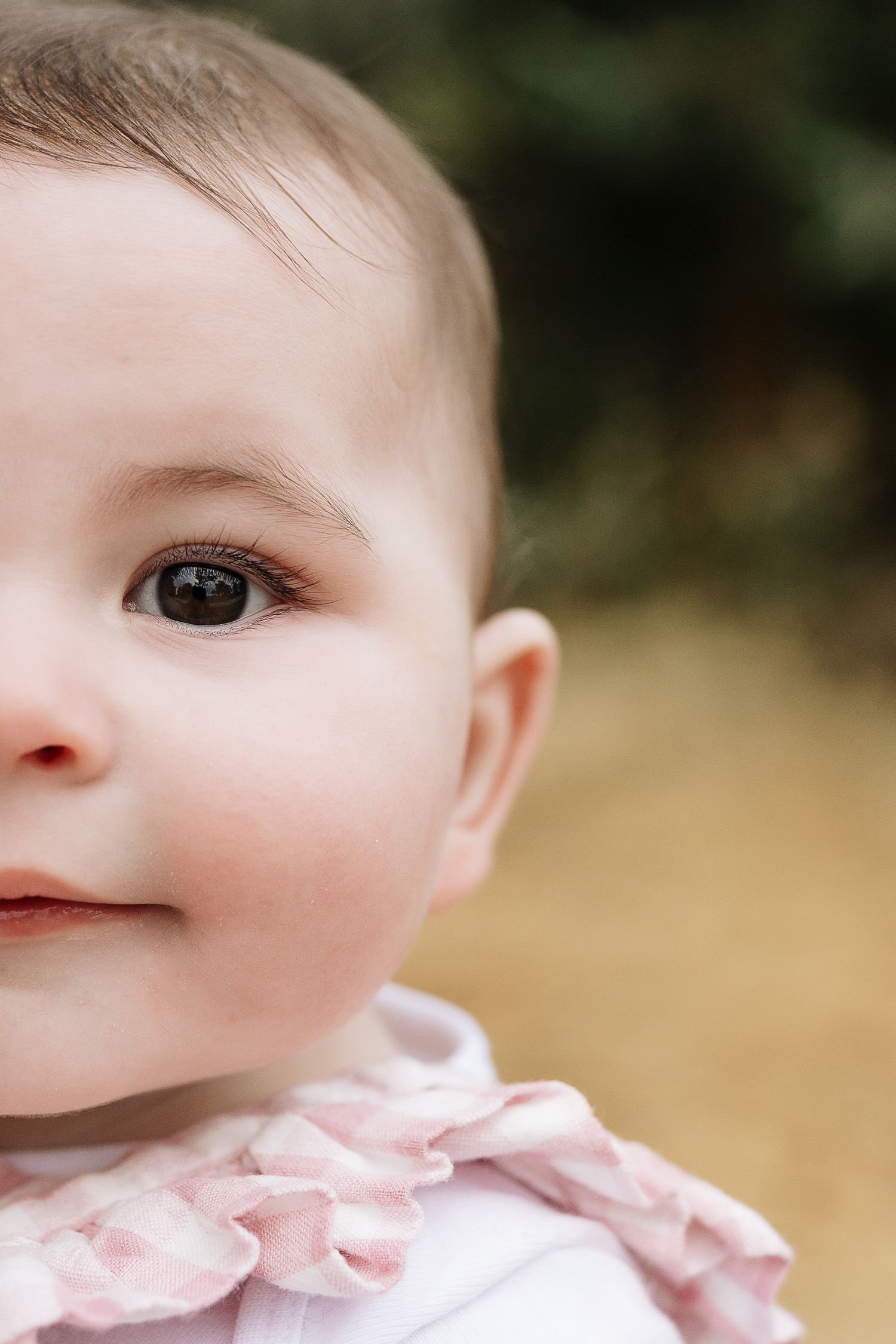 Extreme close-up portrait of baby's face wearing pink collar against blurred outdoor background.