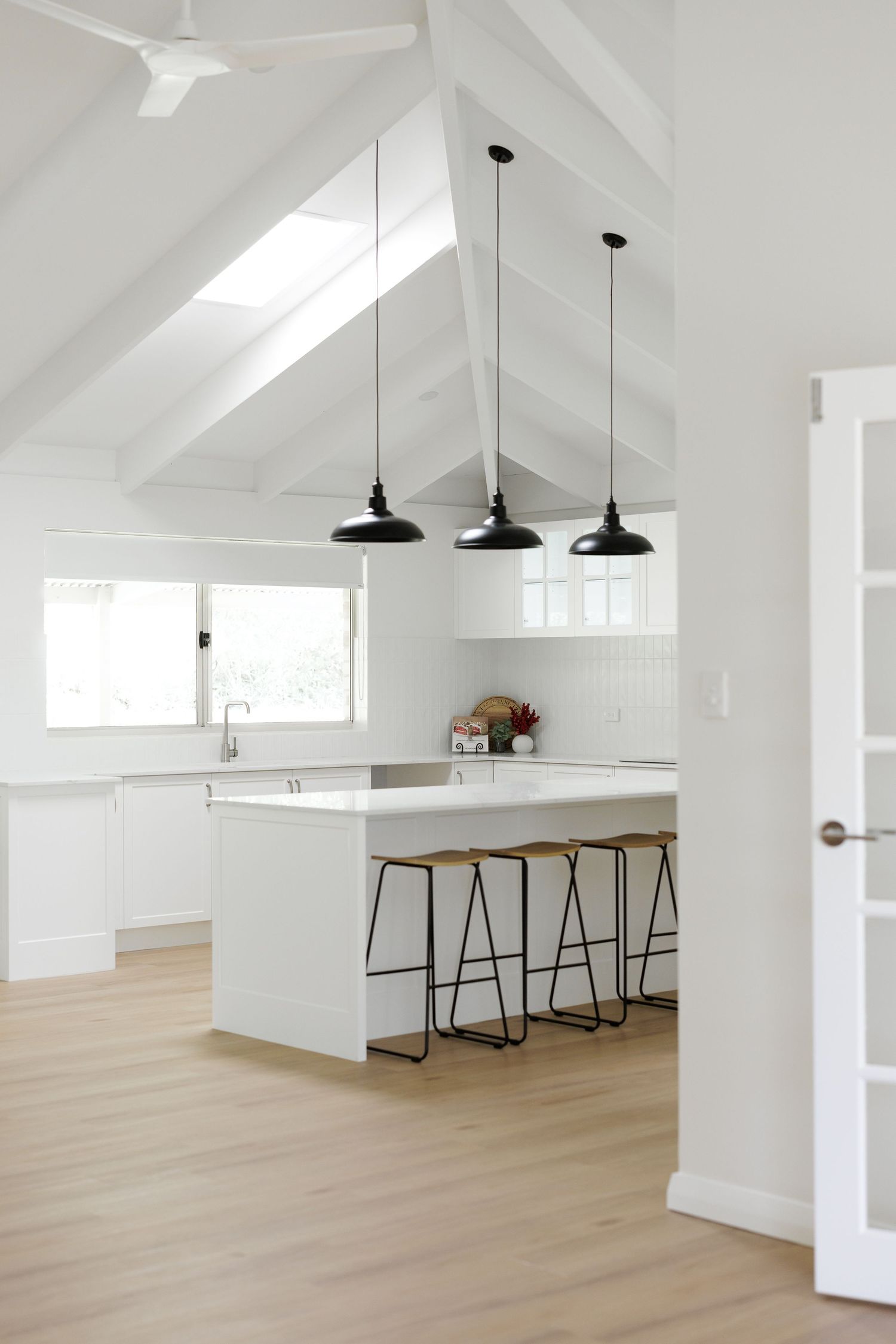 Modern white open concept kitchen with vaulted ceilings, pendant lights, and light wood flooring.