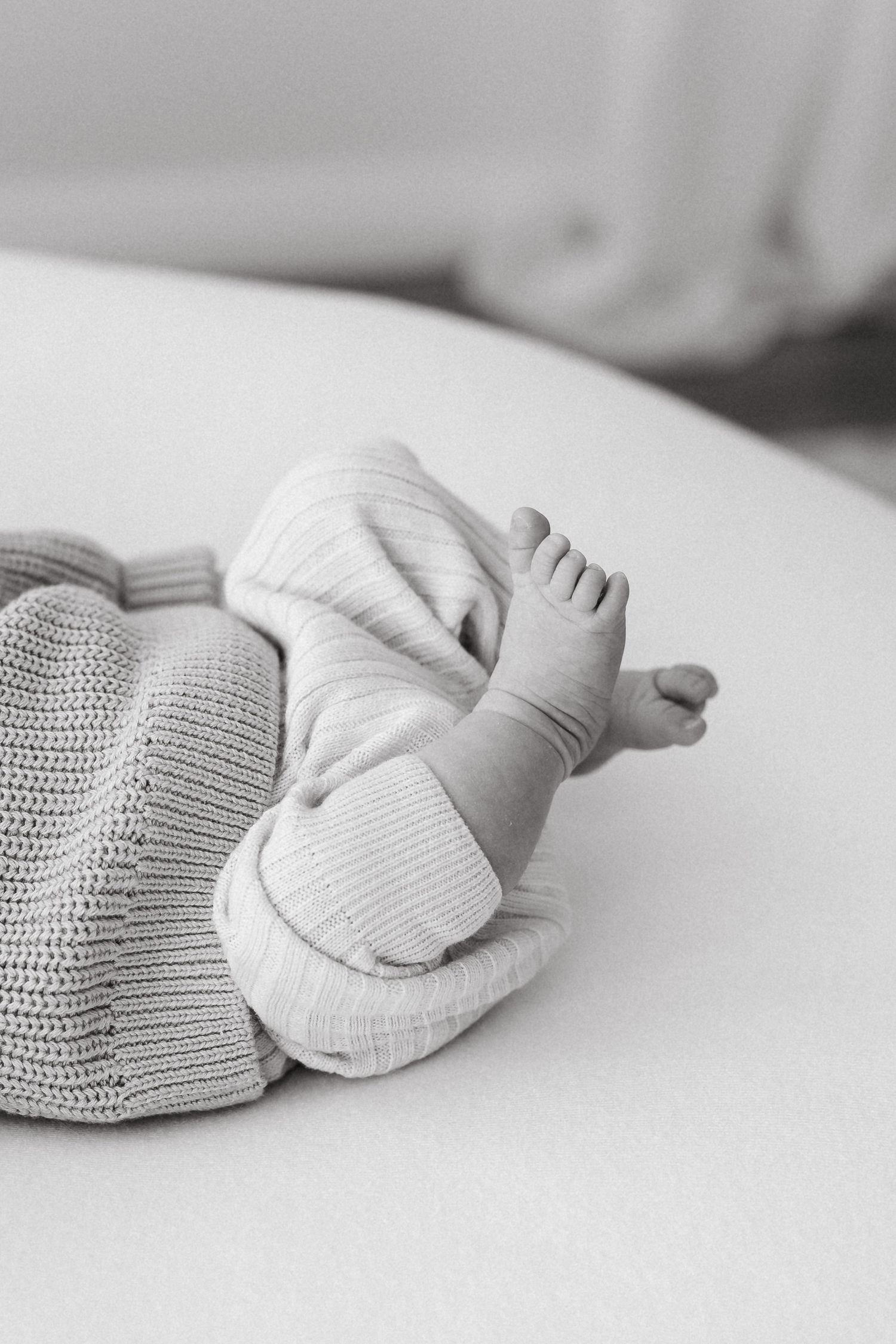 Black and white image of infant feet wearing cozy knit socks on white surface.