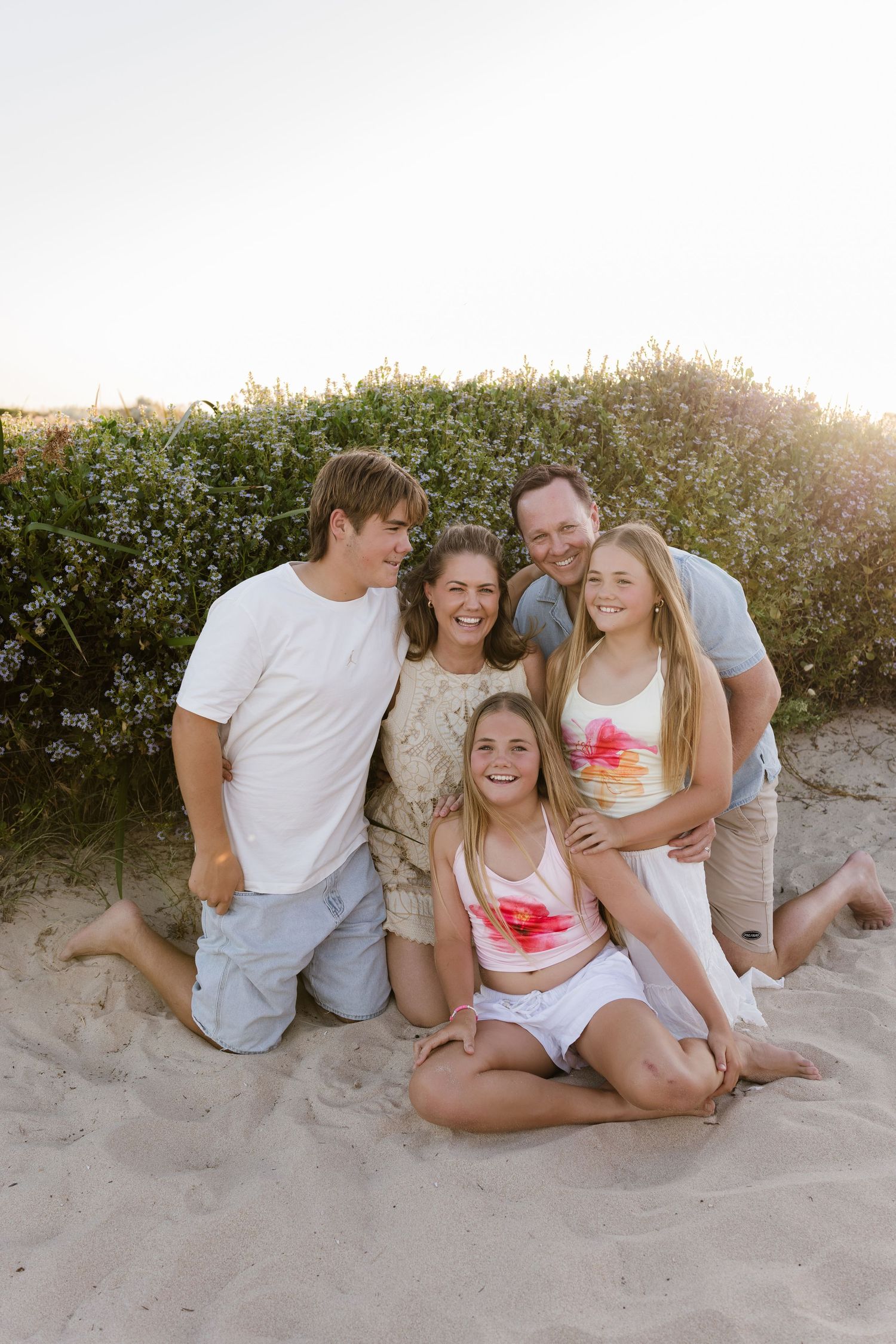Family group relaxing together on sandy beach during golden hour photography session.