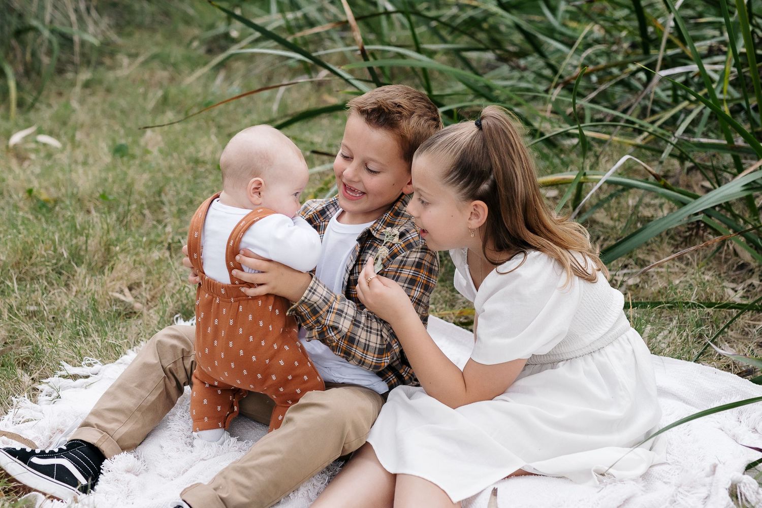 Playful outdoor family moment captured on white blanket with natural backdrop.