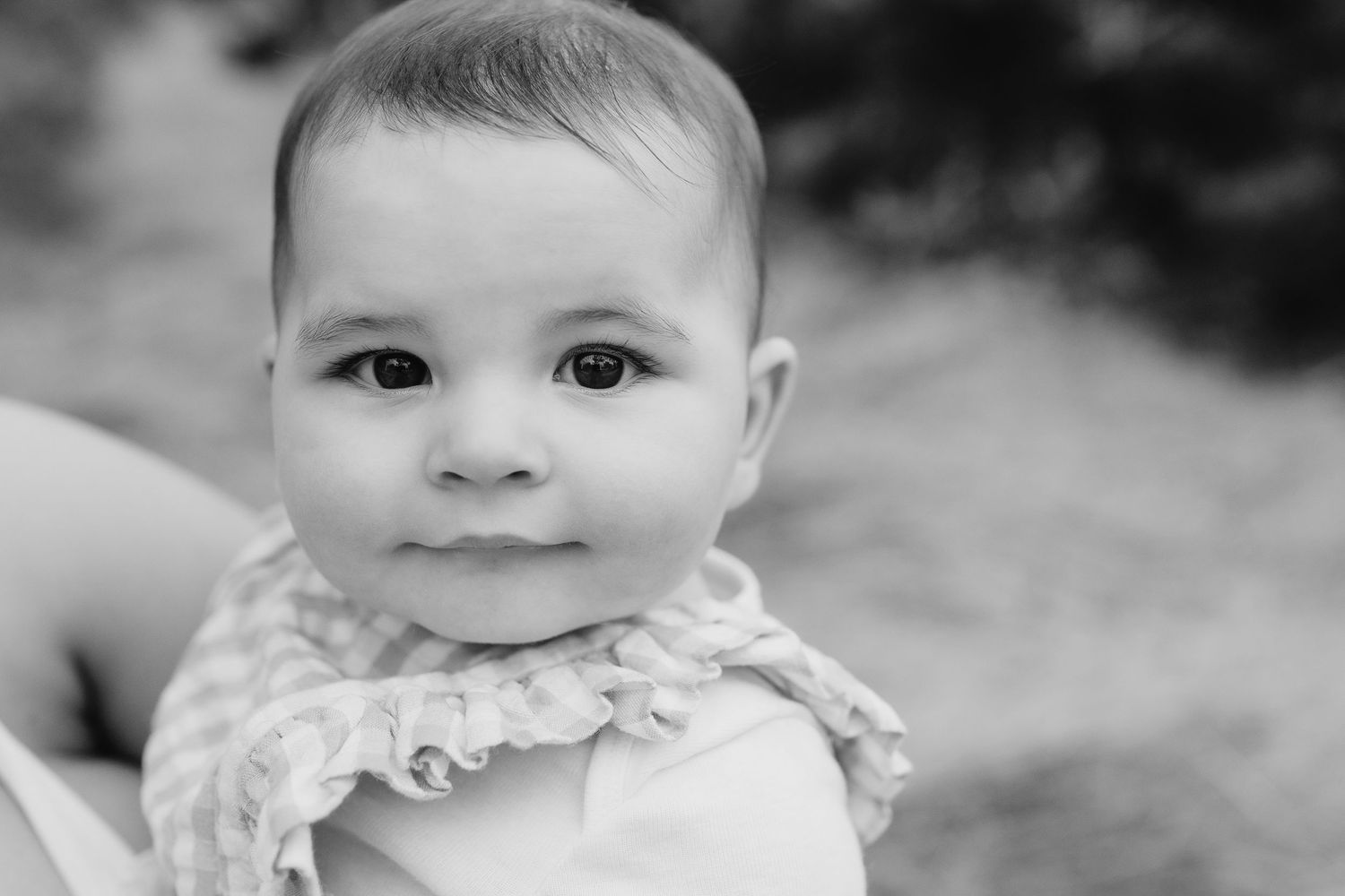 Black and white close-up portrait of smiling baby wearing ruffled collar.