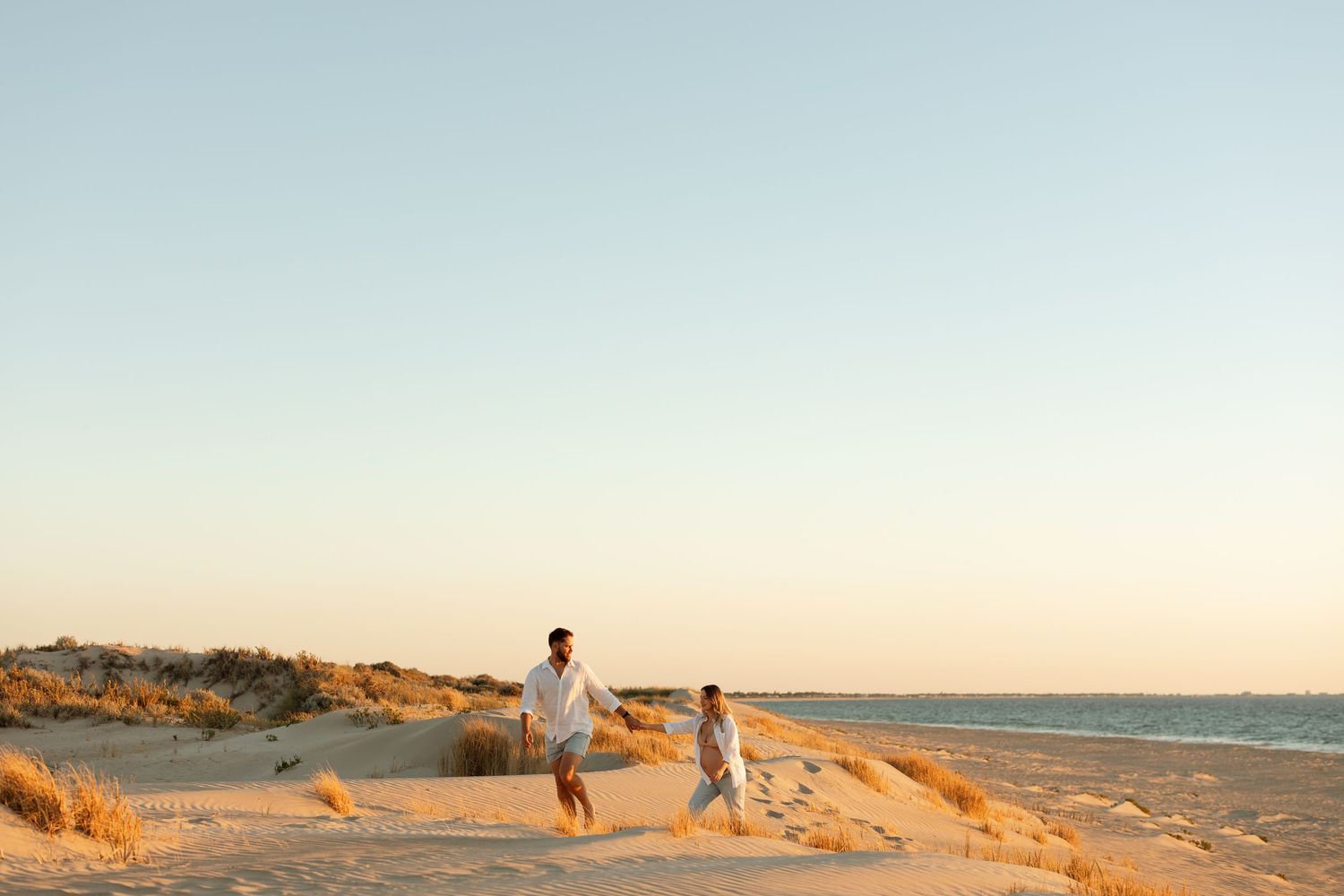 Couple strolling along coastal sand dunes at sunset with ocean view.