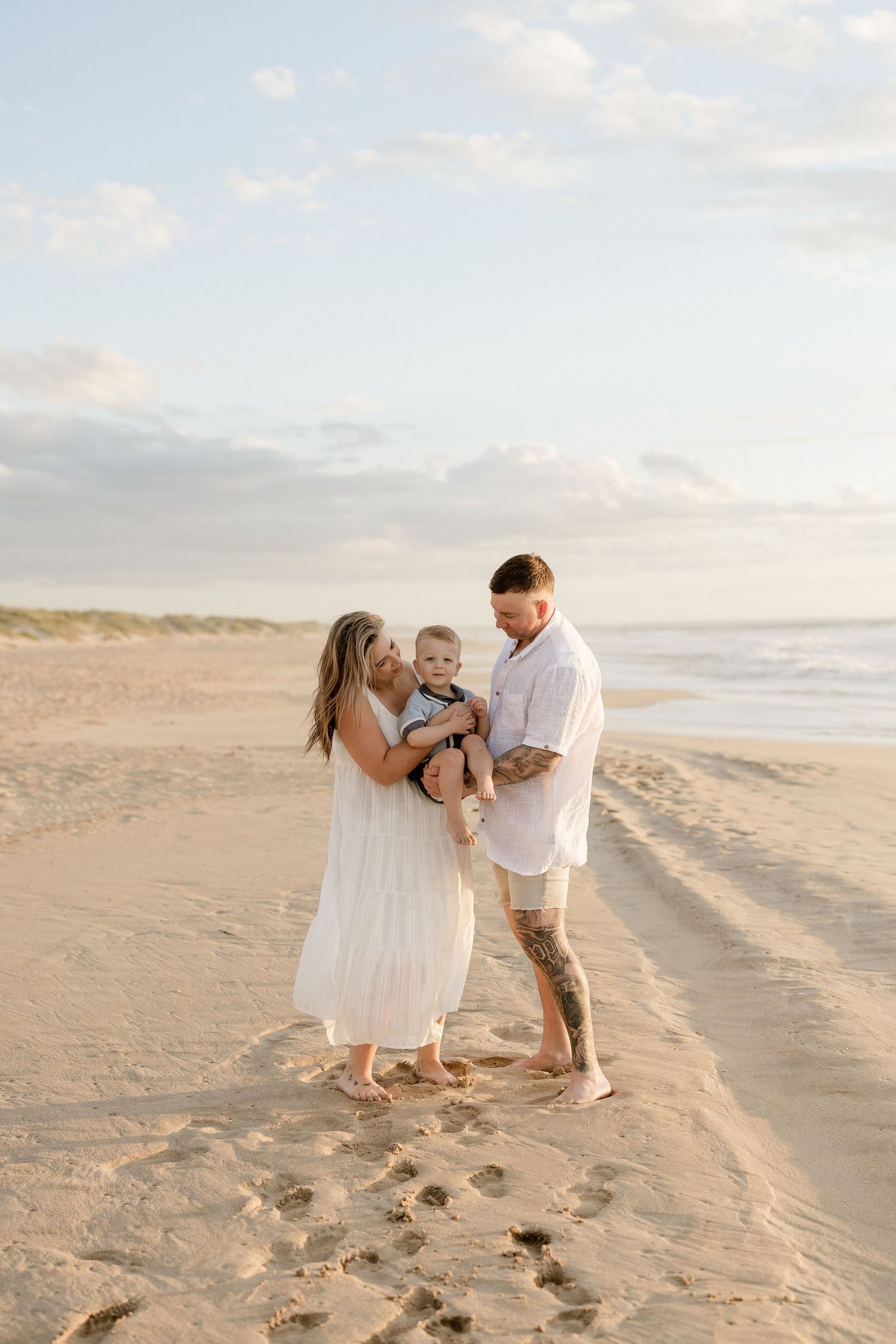 A family stands together on a beach during golden hour with footprints in the sand.