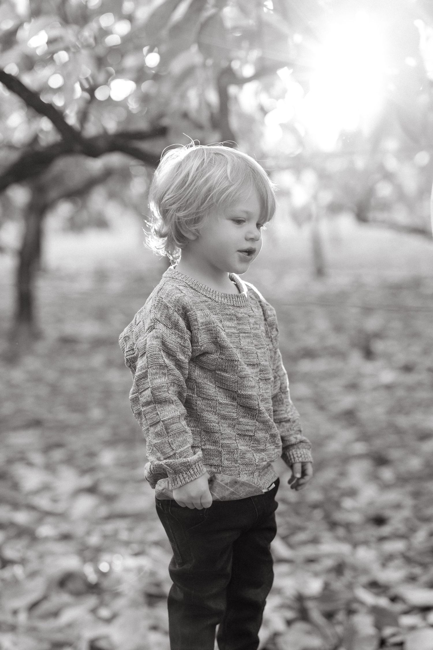 Black and white portrait of young child in knit sweater outdoors.