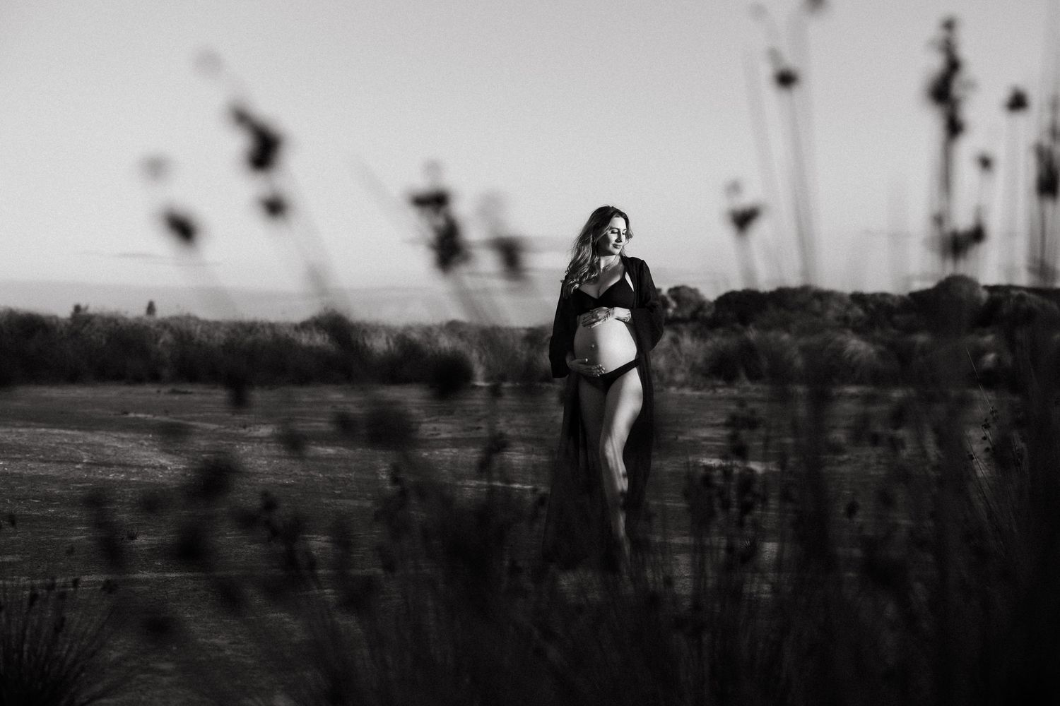 A black and white panoramic sequence showing a person walking through a misty field at dusk.