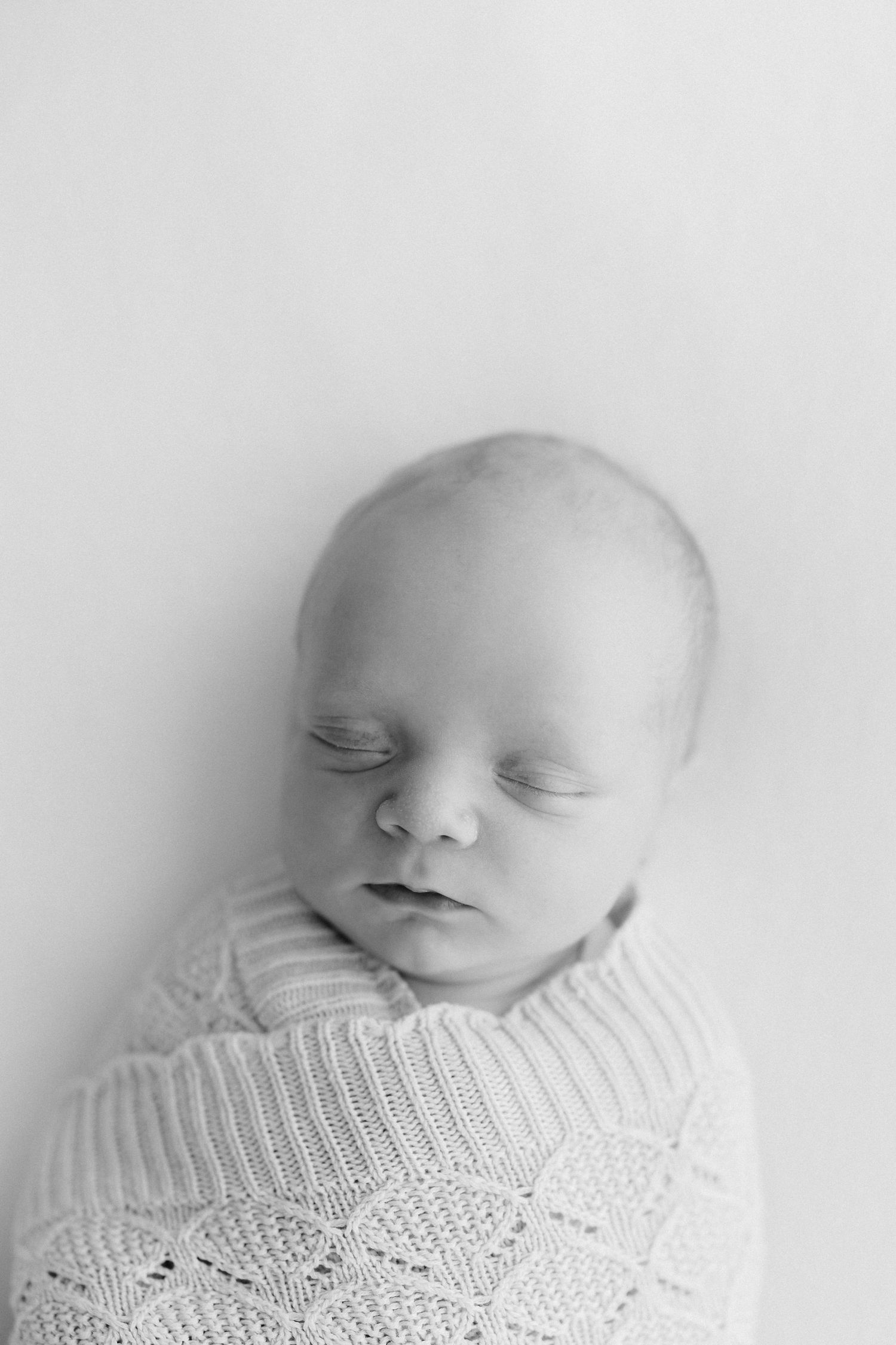 Close-up portraits of sleeping newborn in soft white knit wrap.