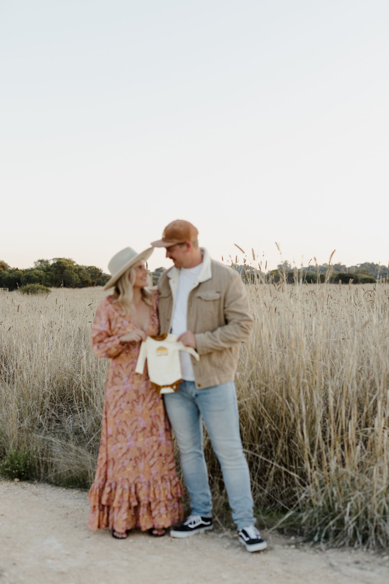 Couple standing together on a dirt path among tall grass during sunset.