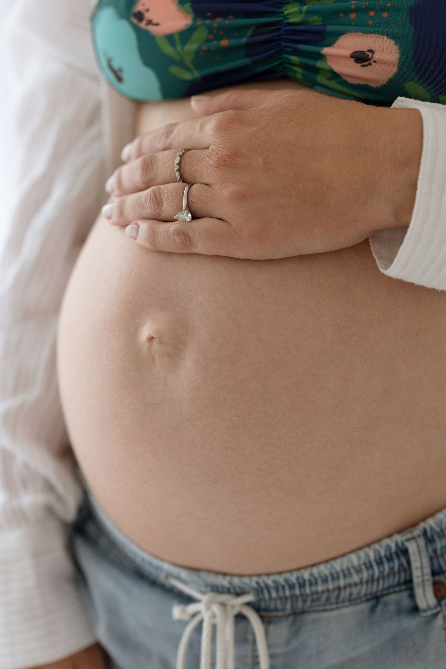 Close-up of pregnant belly with wedding ring visible against floral patterned clothing.