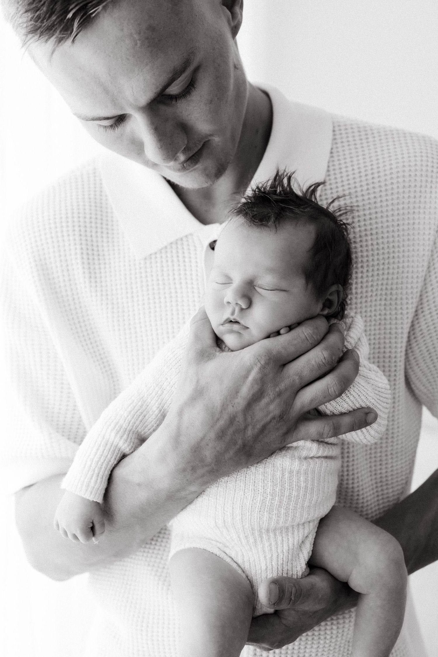 Black and white portrait of gentle embrace between parent and sleeping newborn.