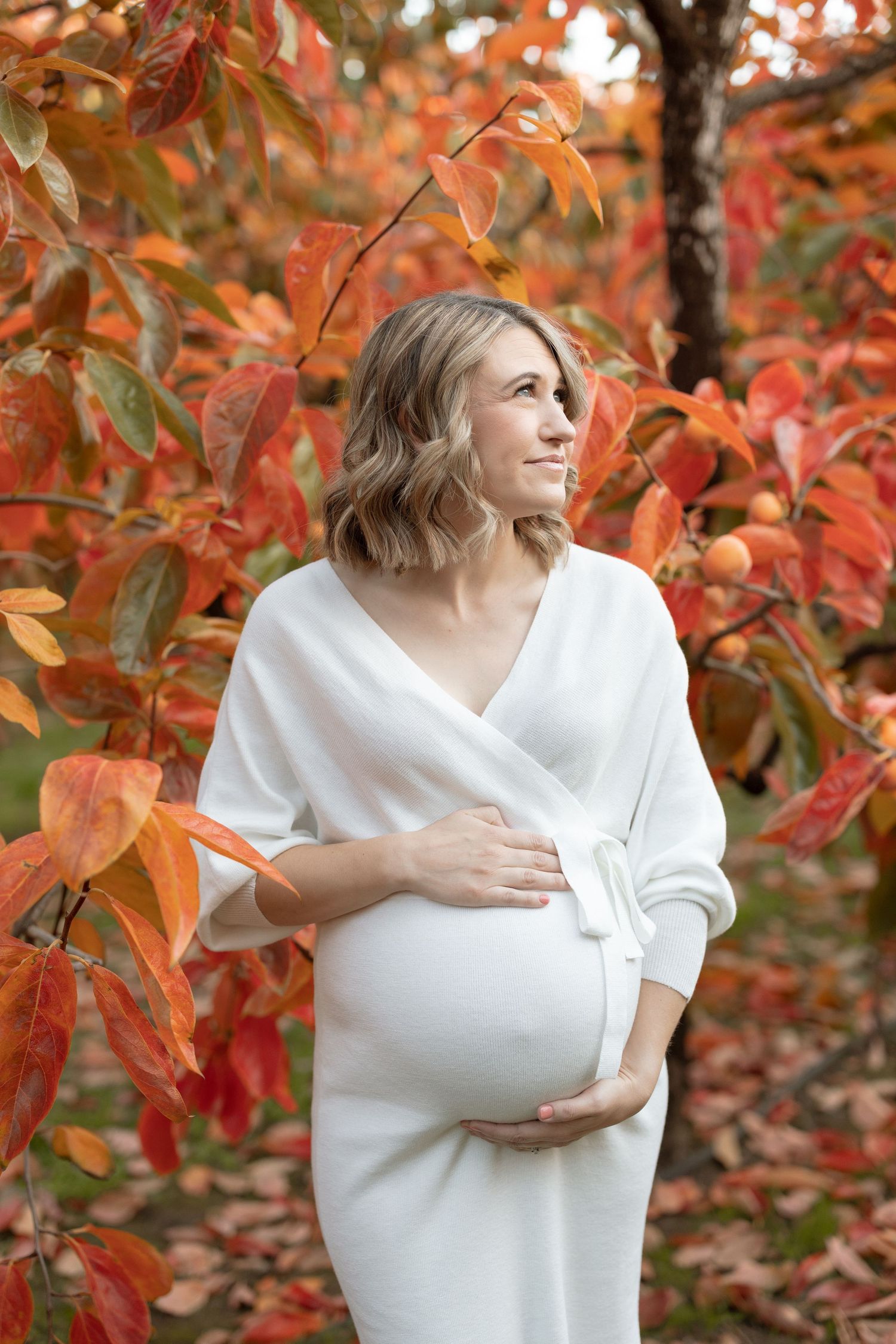 Maternity portrait with white dress against vibrant orange fall leaves.