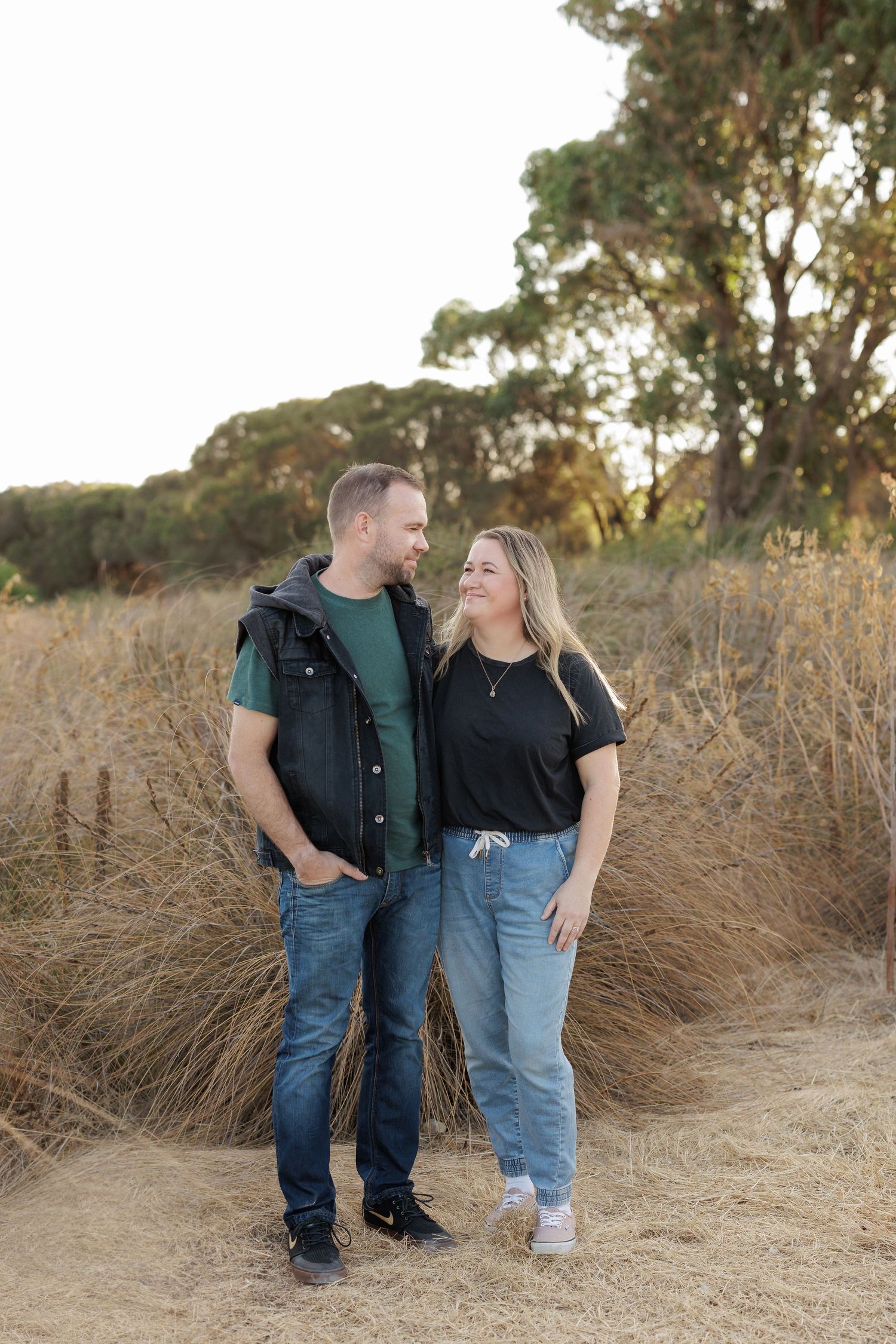 A couple stands together in tall grass during golden hour sharing a loving moment.