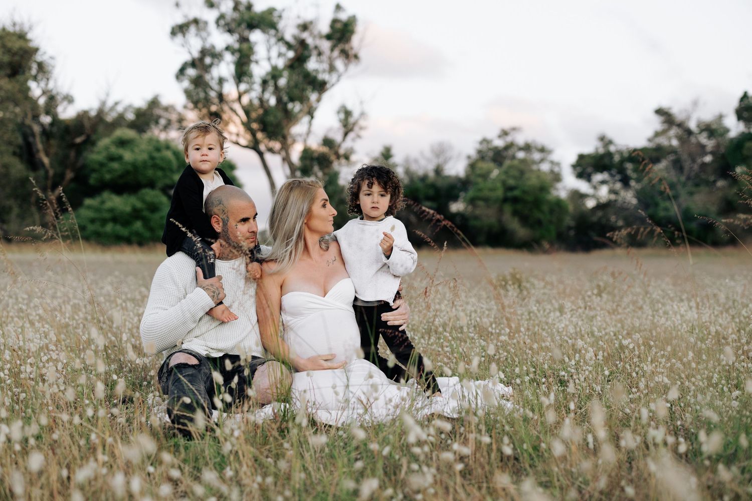 A joyful family moment captured in a sunlit meadow with tall grass and trees.