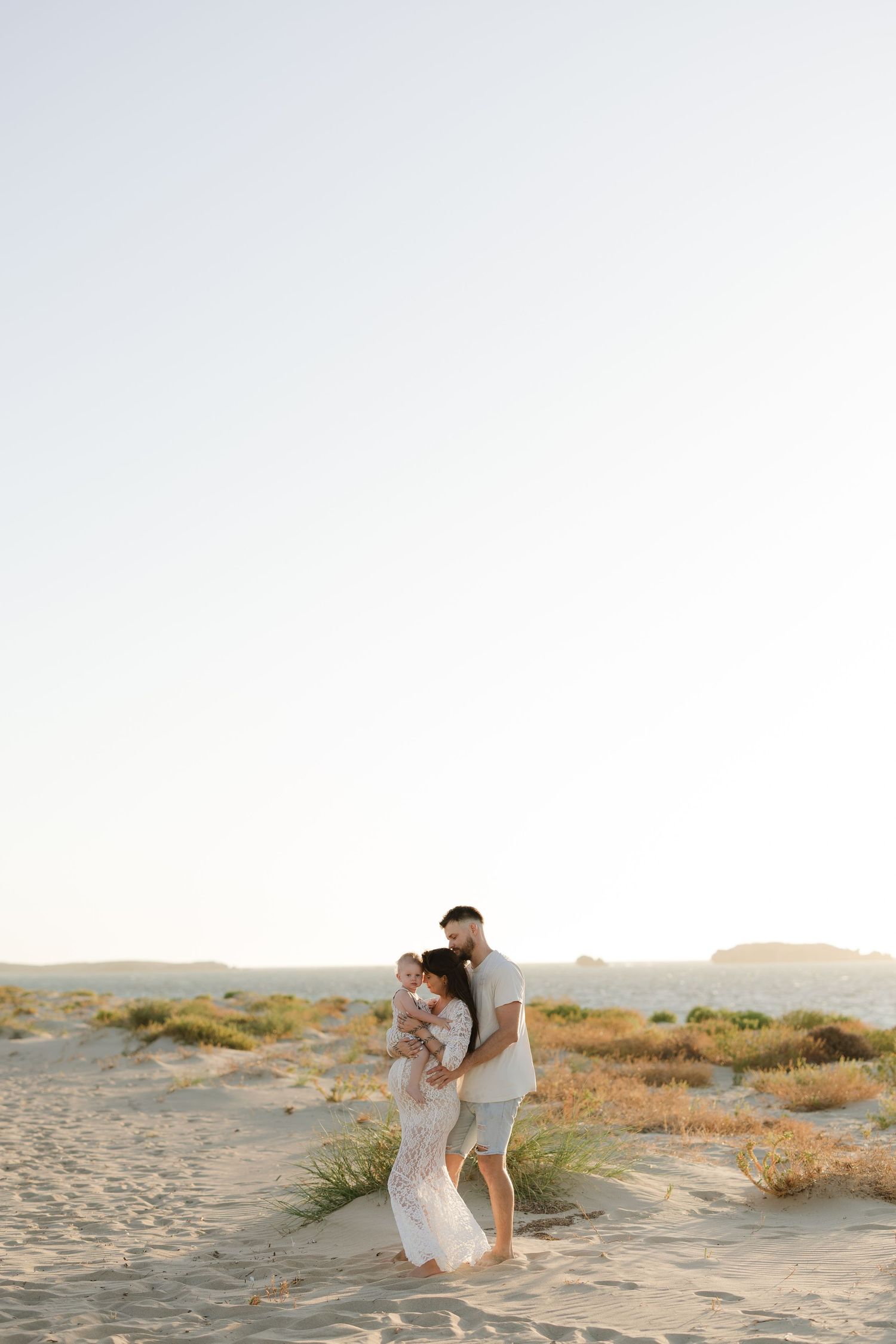 Couple sharing romantic moment on beach during sunset maternity photoshoot.