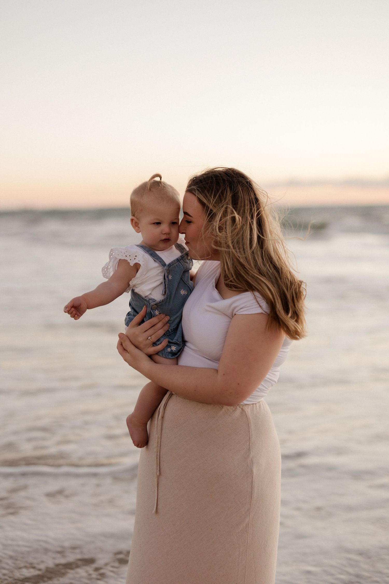 Tender family moment shared on a beach at sunset with ocean waves in background.