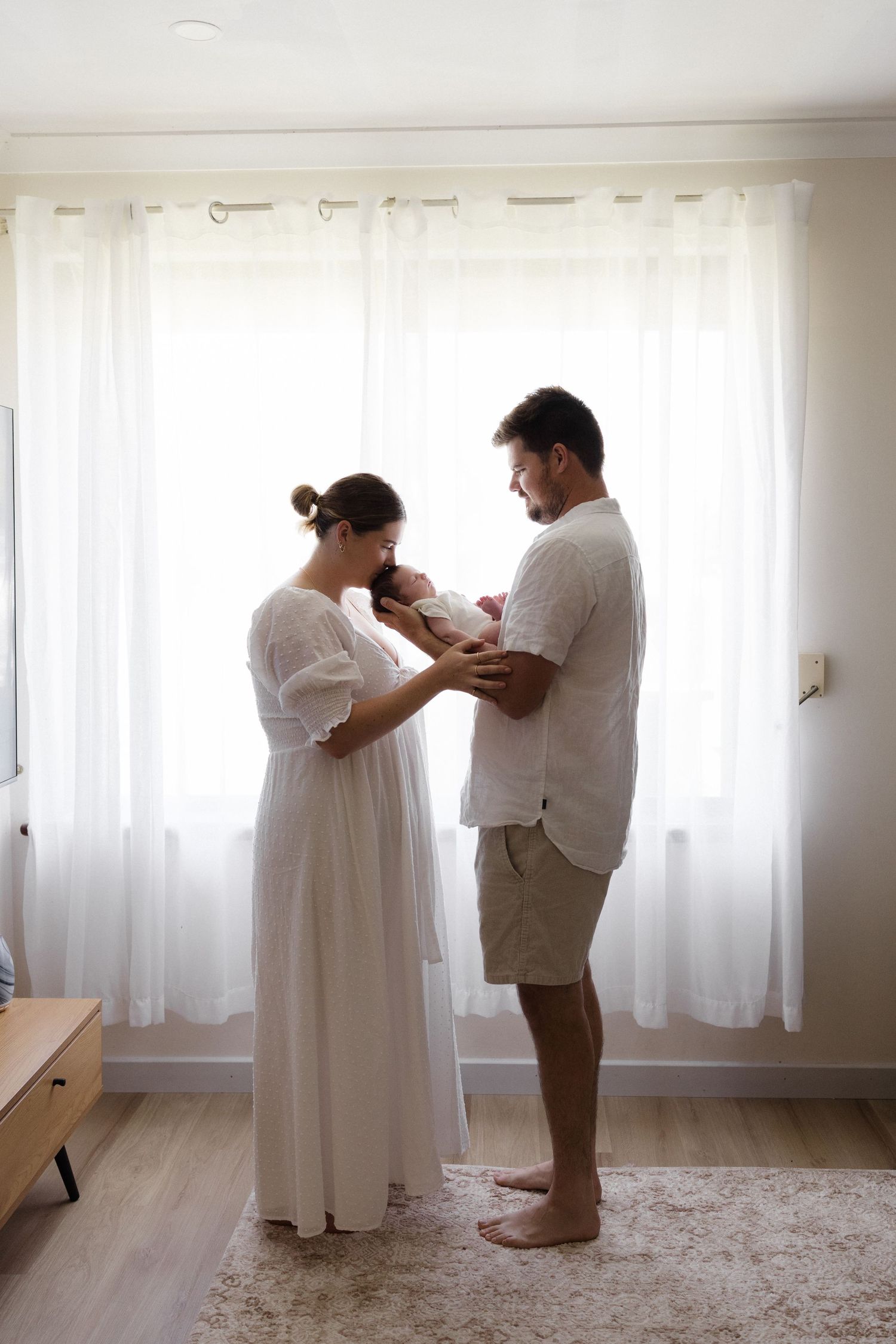 Family photoshoot in bright room with white curtains and carpet.