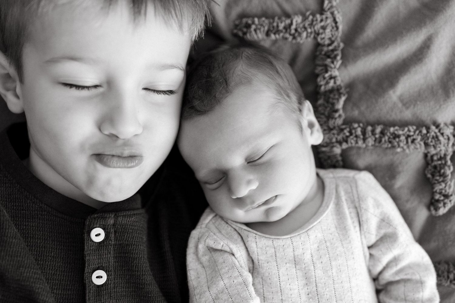 Two children resting peacefully on textured gray bedding in black and white.