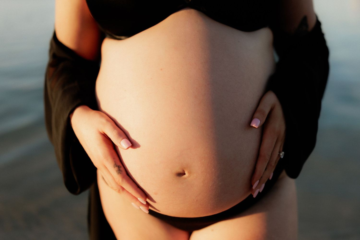 Silhouette of pregnant belly against sunset sky at beach.
